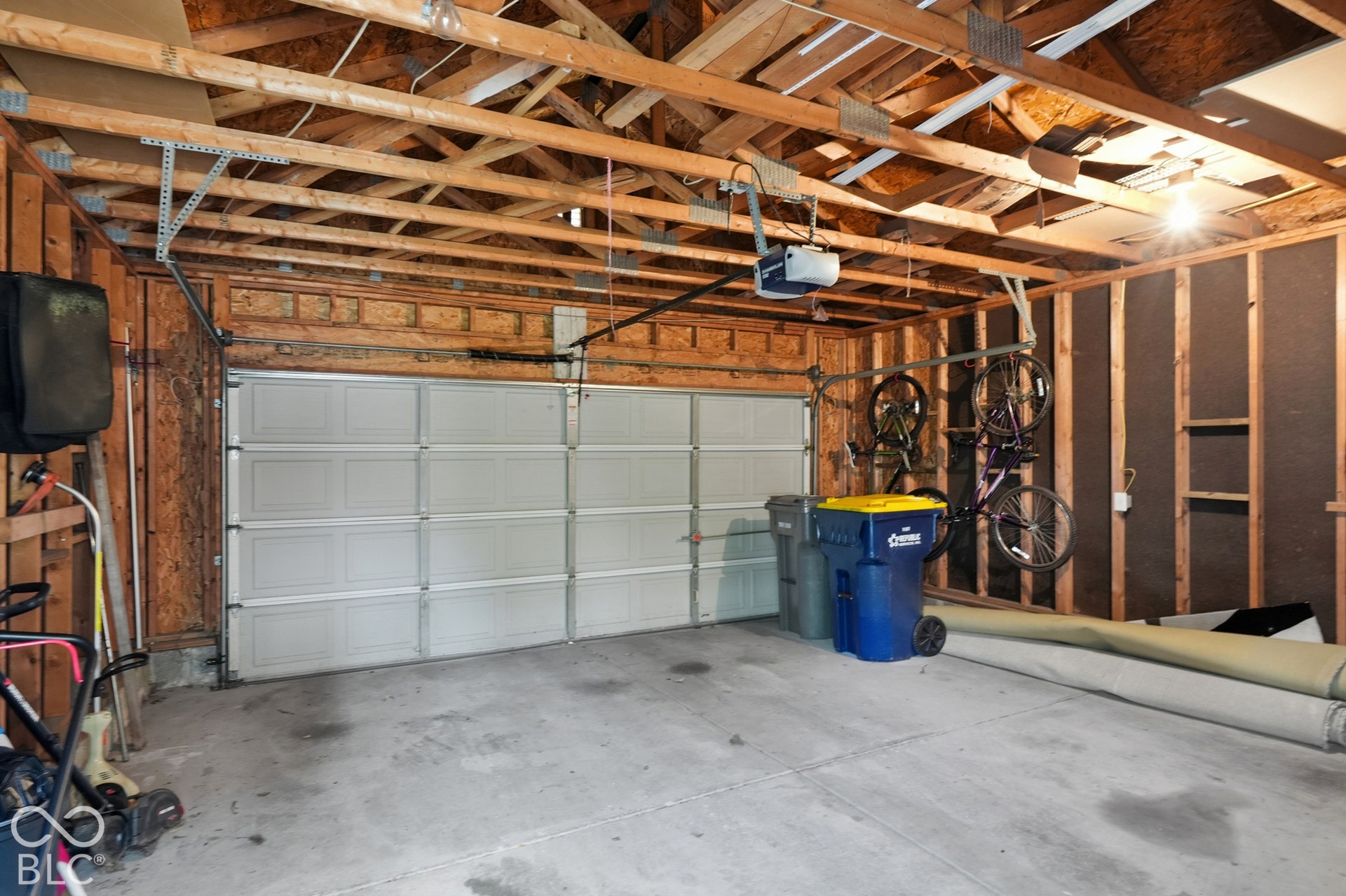 Garage space featuring a paneled overhead door, exposed wood framing, and concrete flooring