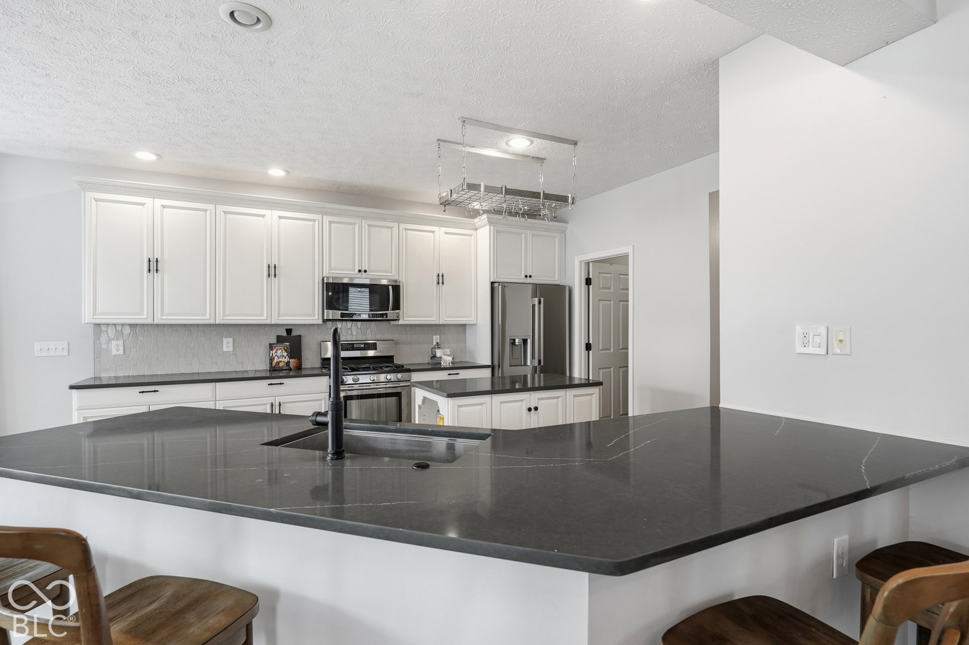 Kitchen featuring a large central island with sink, dark countertops, white shaker-style cabinetry, and stainless steel appliances