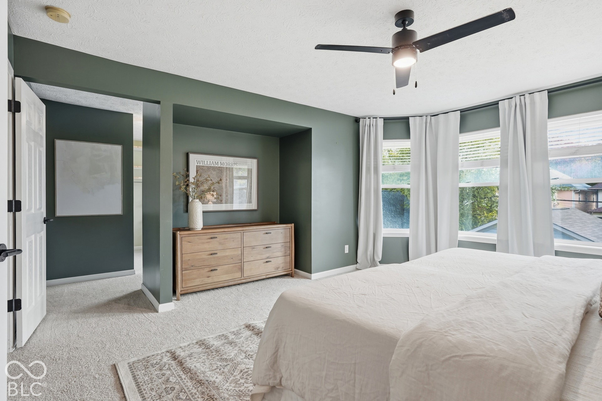 Plush carpeting, a modern ceiling fan with lighting, multiple windows with blinds, and white doors with matte black hardware