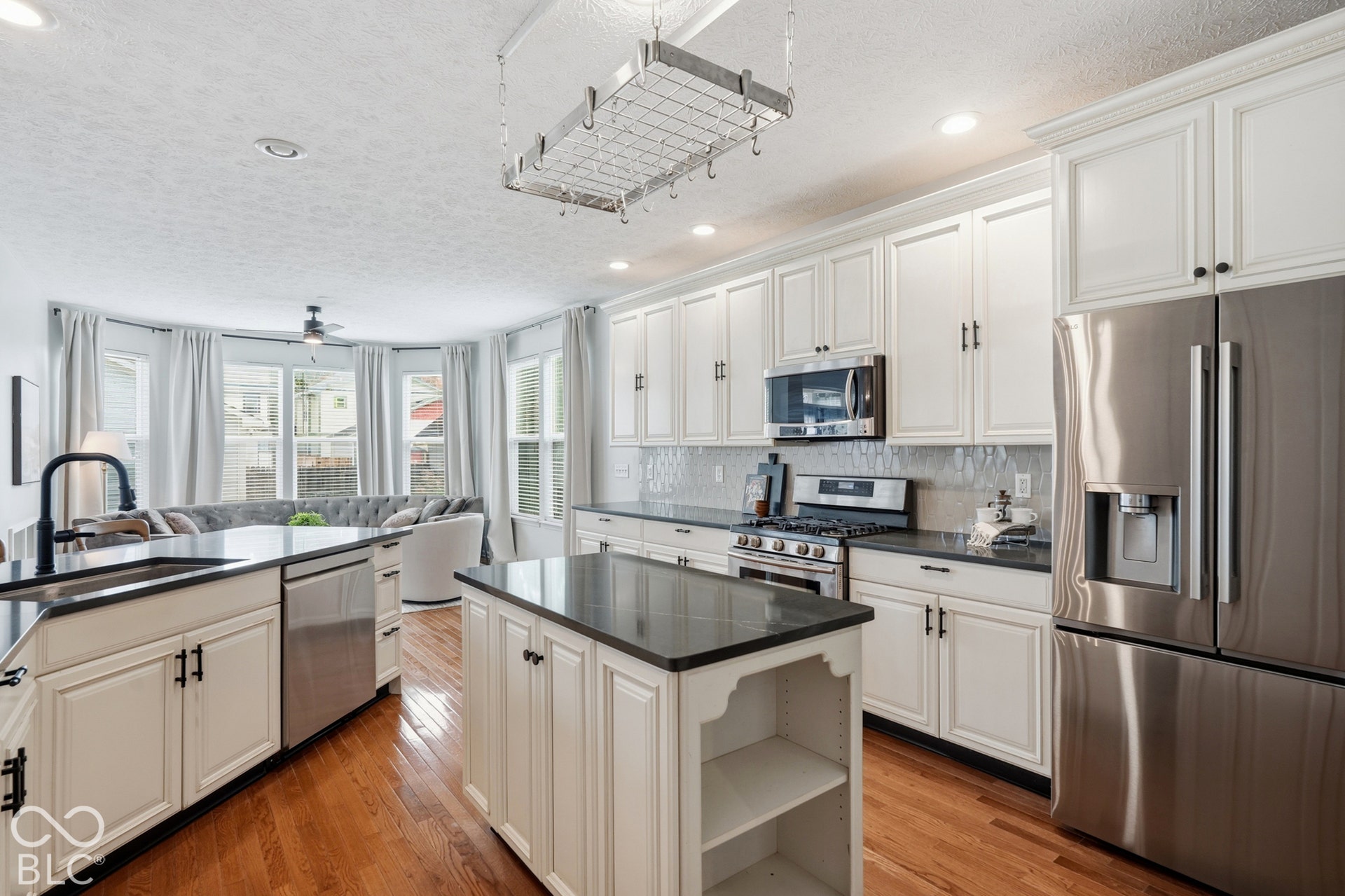Kitchen featuring white cabinetry with dark hardware, dark countertops, stainless steel appliances, and hardwood flooring