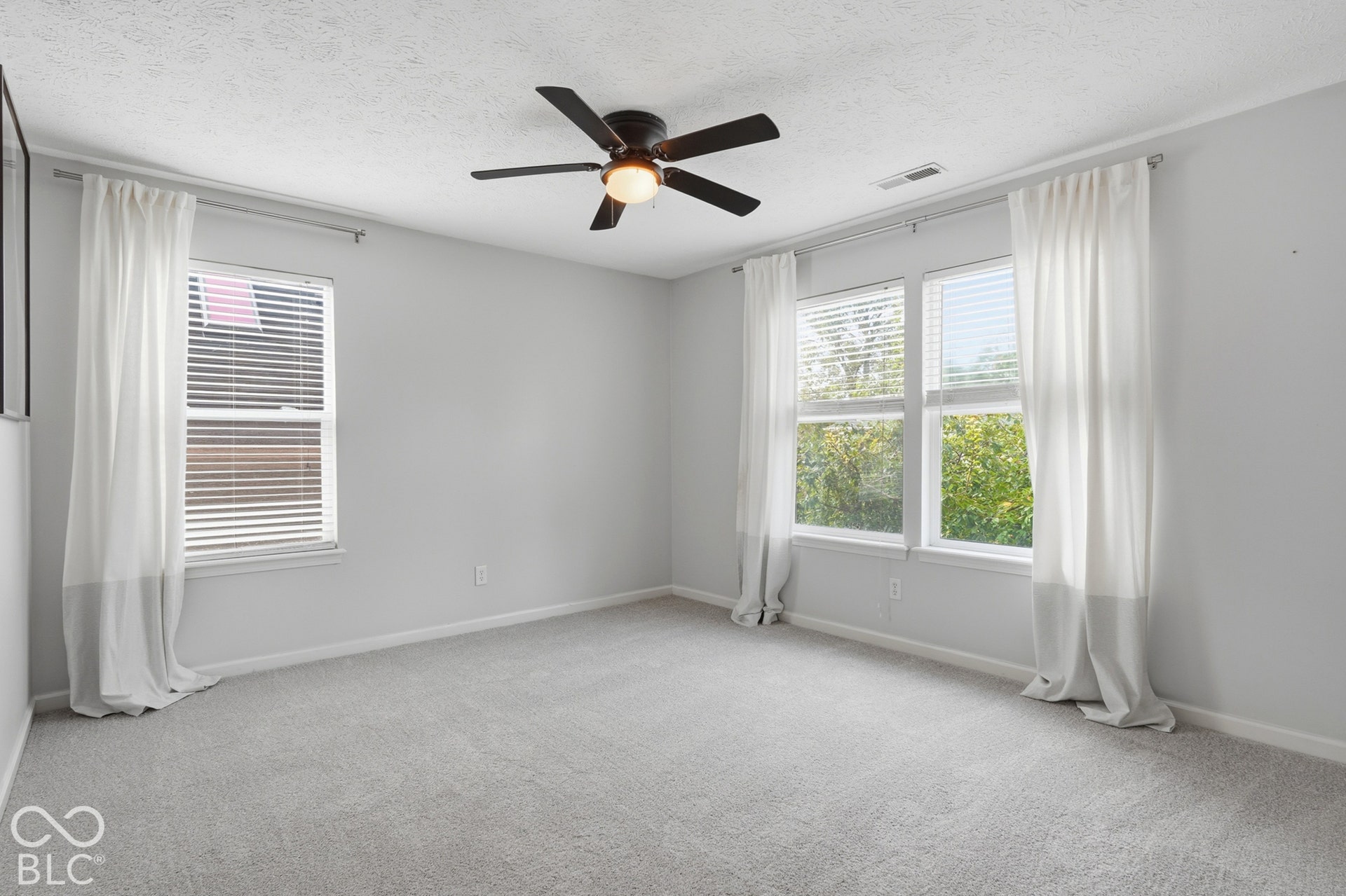 Plush carpet flooring, multiple windows with blinds, ceiling fan with integrated lighting, and neutral wall tones