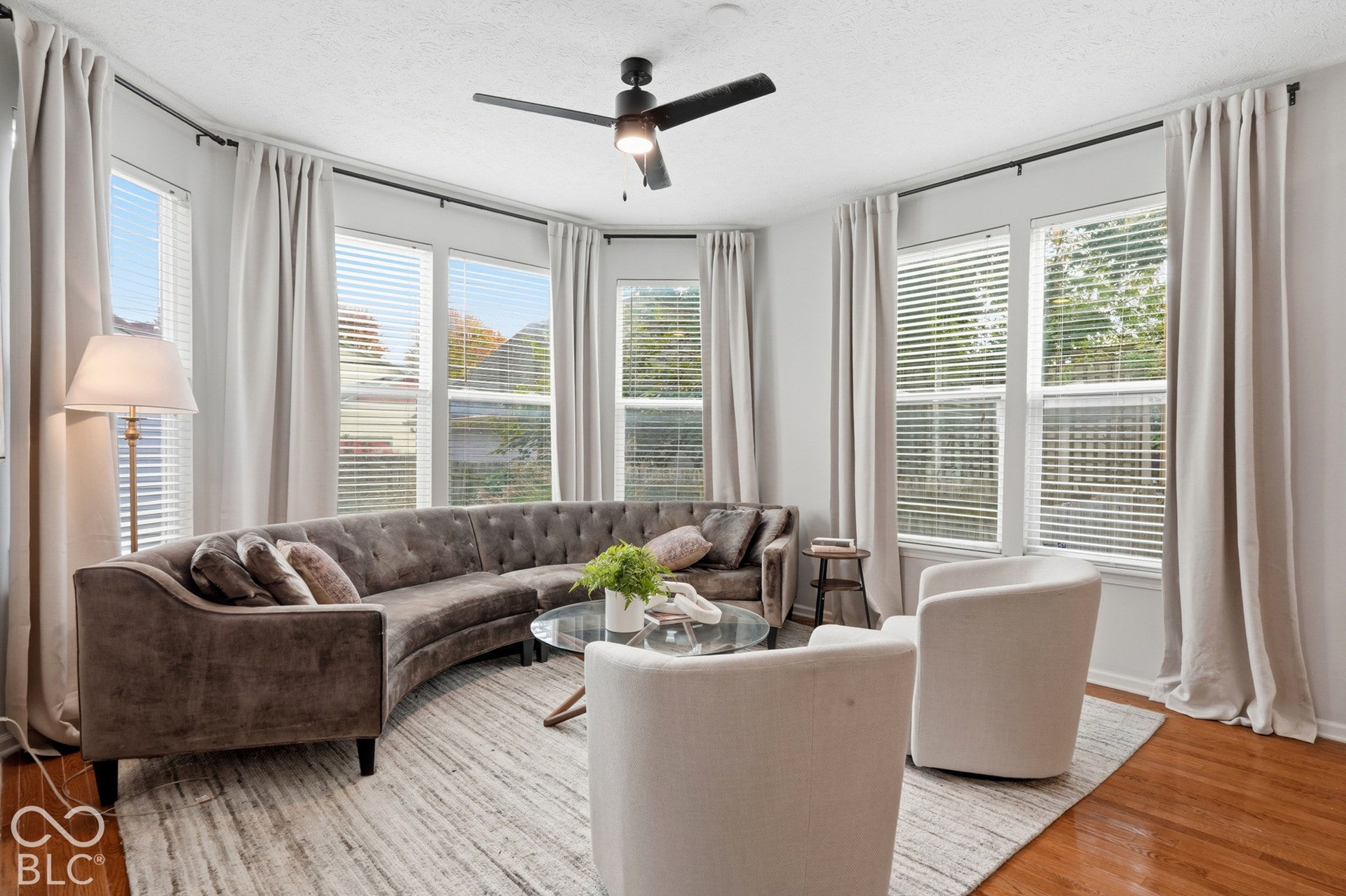 Bay window configuration, hardwood flooring, ceiling fan, and multiple windows with blinds