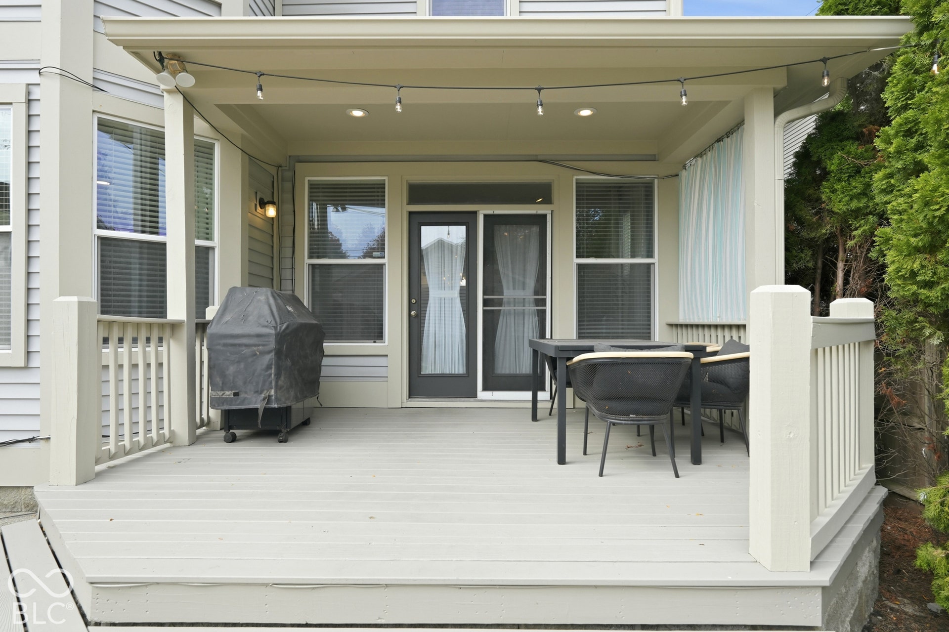 Covered outdoor deck with light gray wood-finish decking, white railings, and a sliding glass door