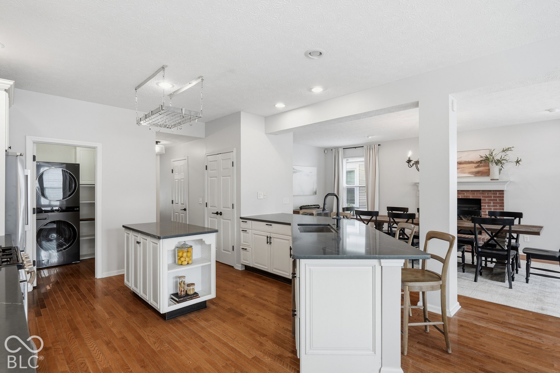 Kitchen featuring hardwood flooring, white cabinetry, dark countertops, a center island with open shelving, and a pot rack