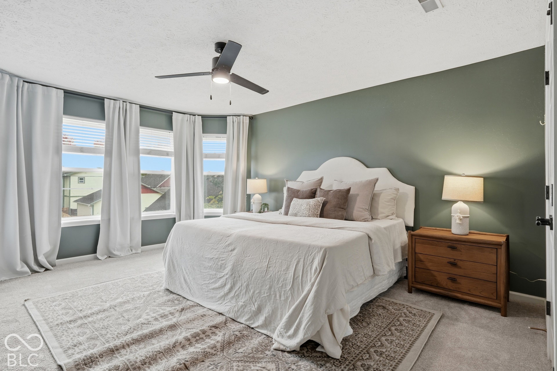 Curved wall with multiple windows, recessed lighting, ceiling fan with integrated lighting, soft green accent wall, and neutral-toned carpeting