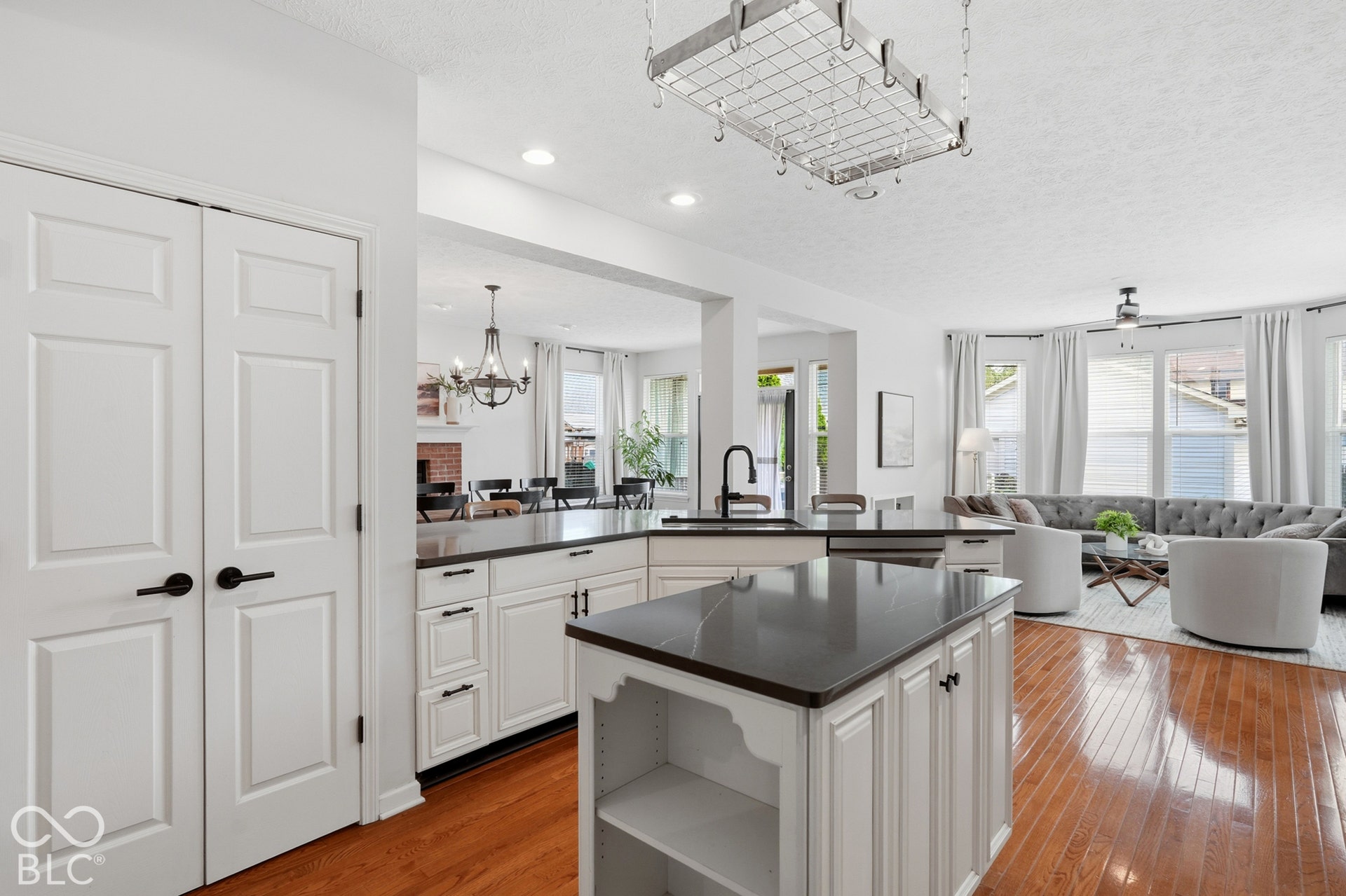 White shaker cabinetry, dark countertops, hardwood flooring, recessed lighting, and a pot rack