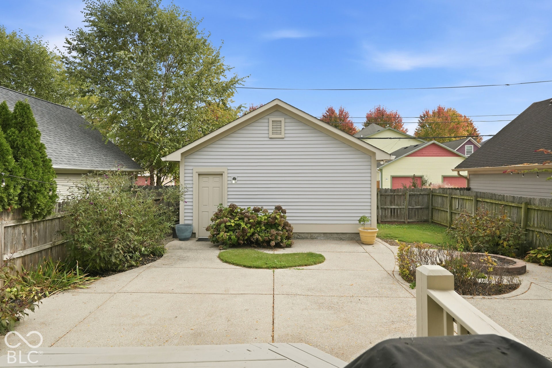 Expansive concrete patio with integrated circular lawn area, wood privacy fencing, and mature perimeter landscaping