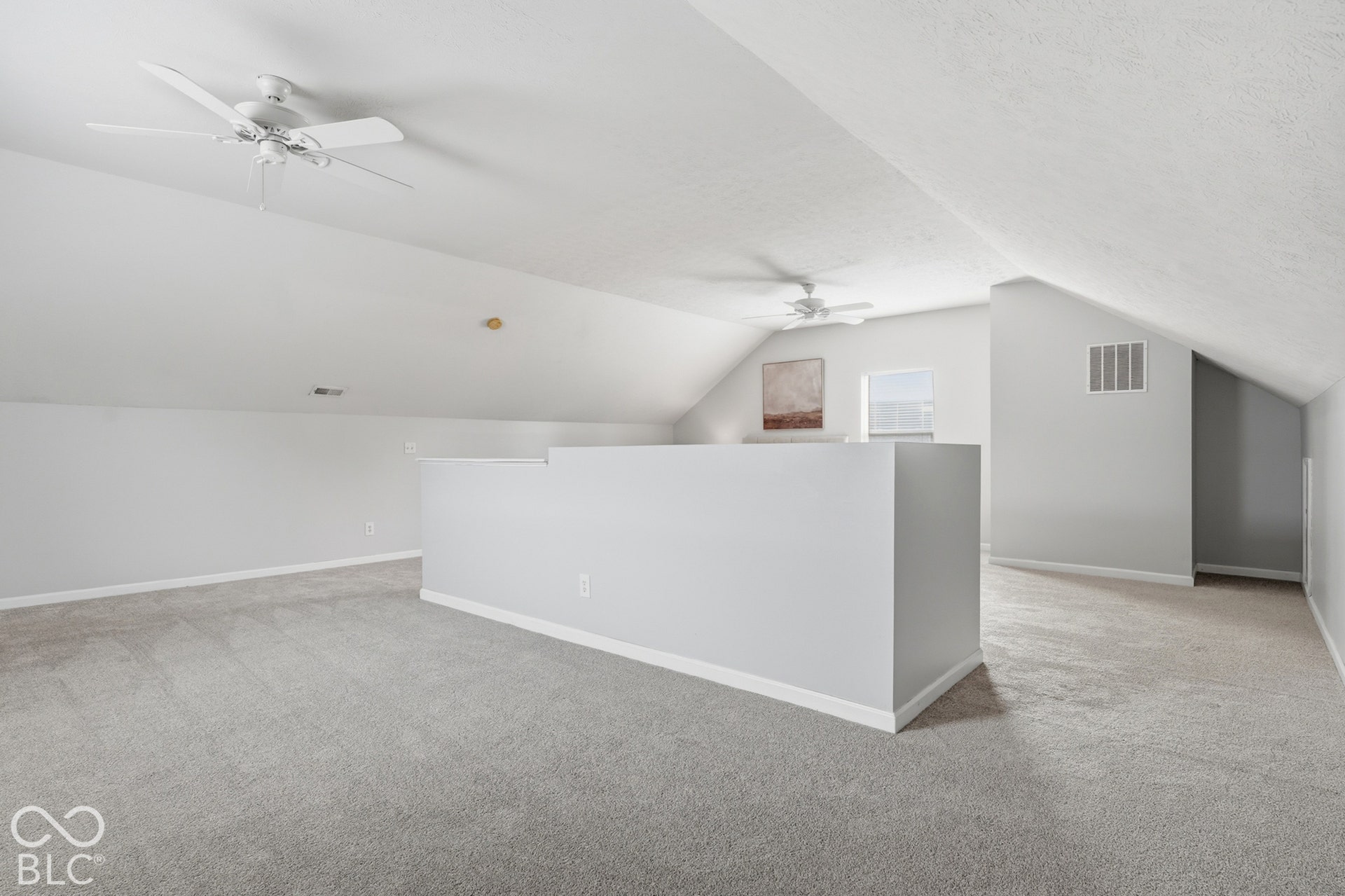 Carpeted open loft space with angled ceilings, two ceiling fans, and a window