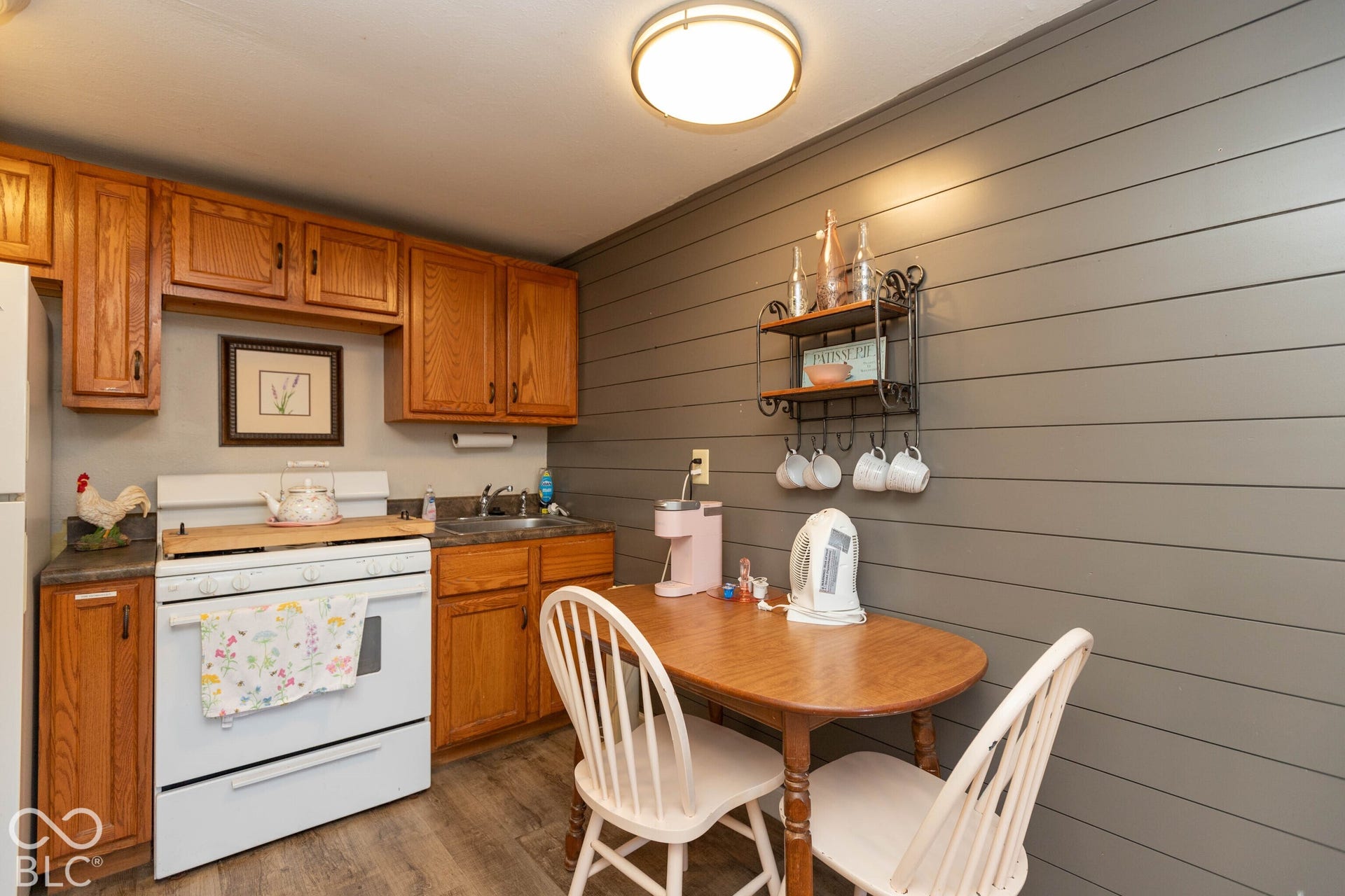 Wood-finish flooring, wood cabinetry, built-in shelving, a kitchen sink, and a white oven/range