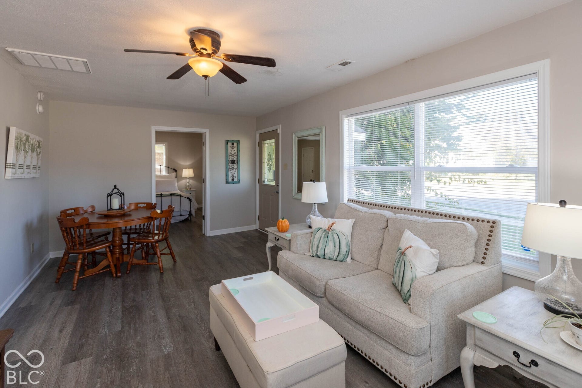 Wood-finish flooring, ceiling fan with integrated lighting, large window with blinds, light neutral wall paint, and white trim