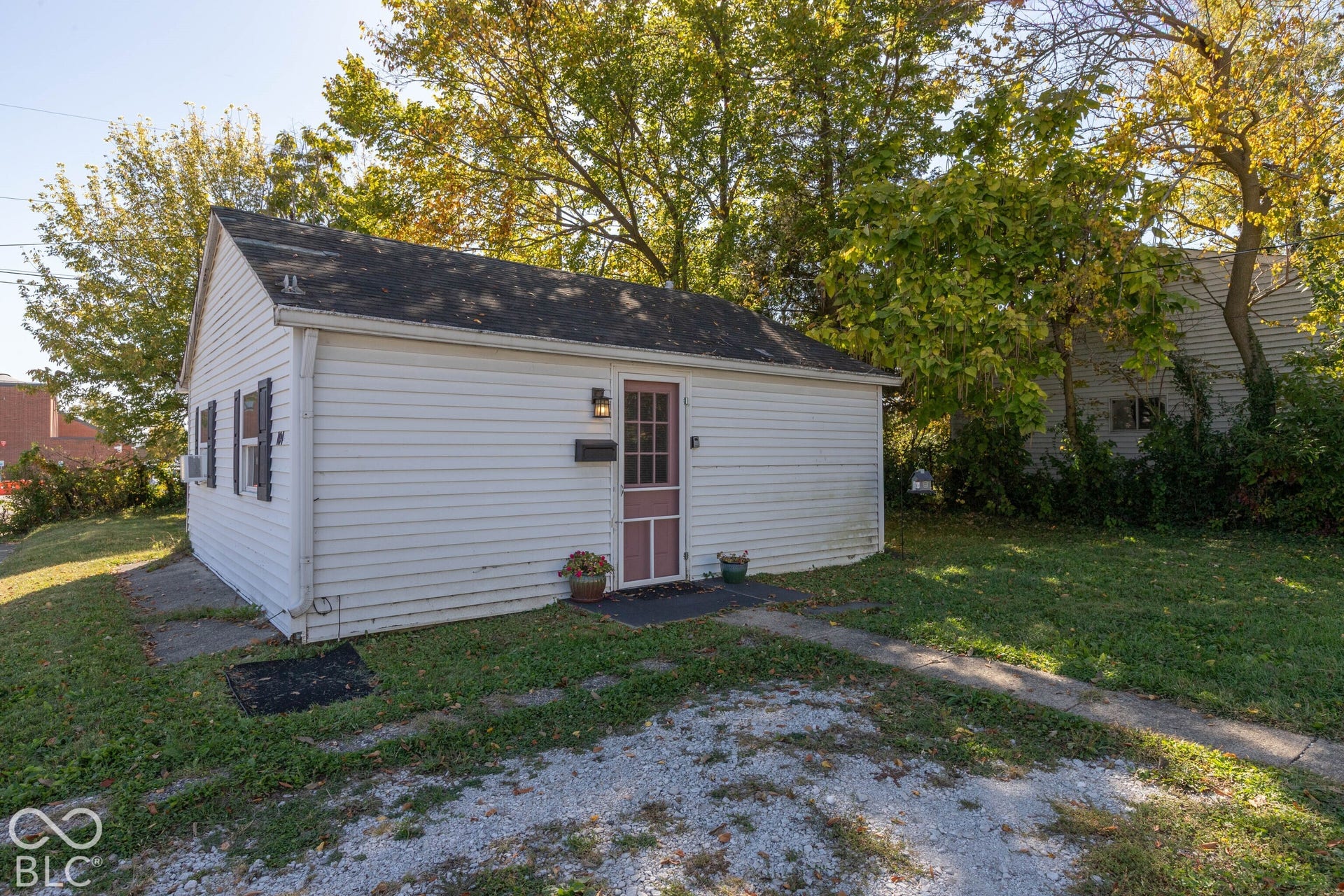 White siding exterior with a dark-paneled door, black exterior light fixture, and black louvered shutters