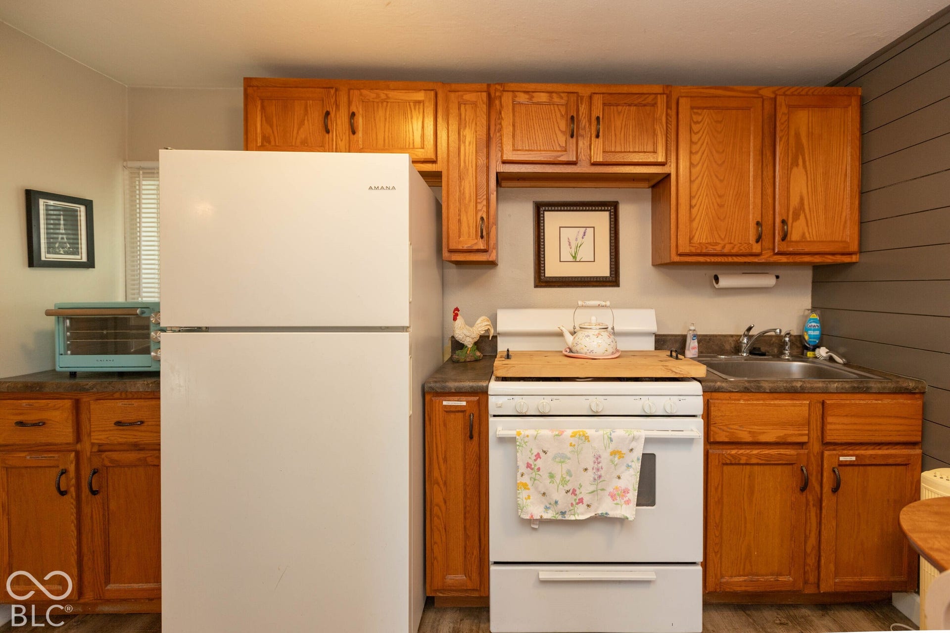Wood-finish cabinetry, solid surface countertops, white refrigerator, white range, and a stainless steel sink