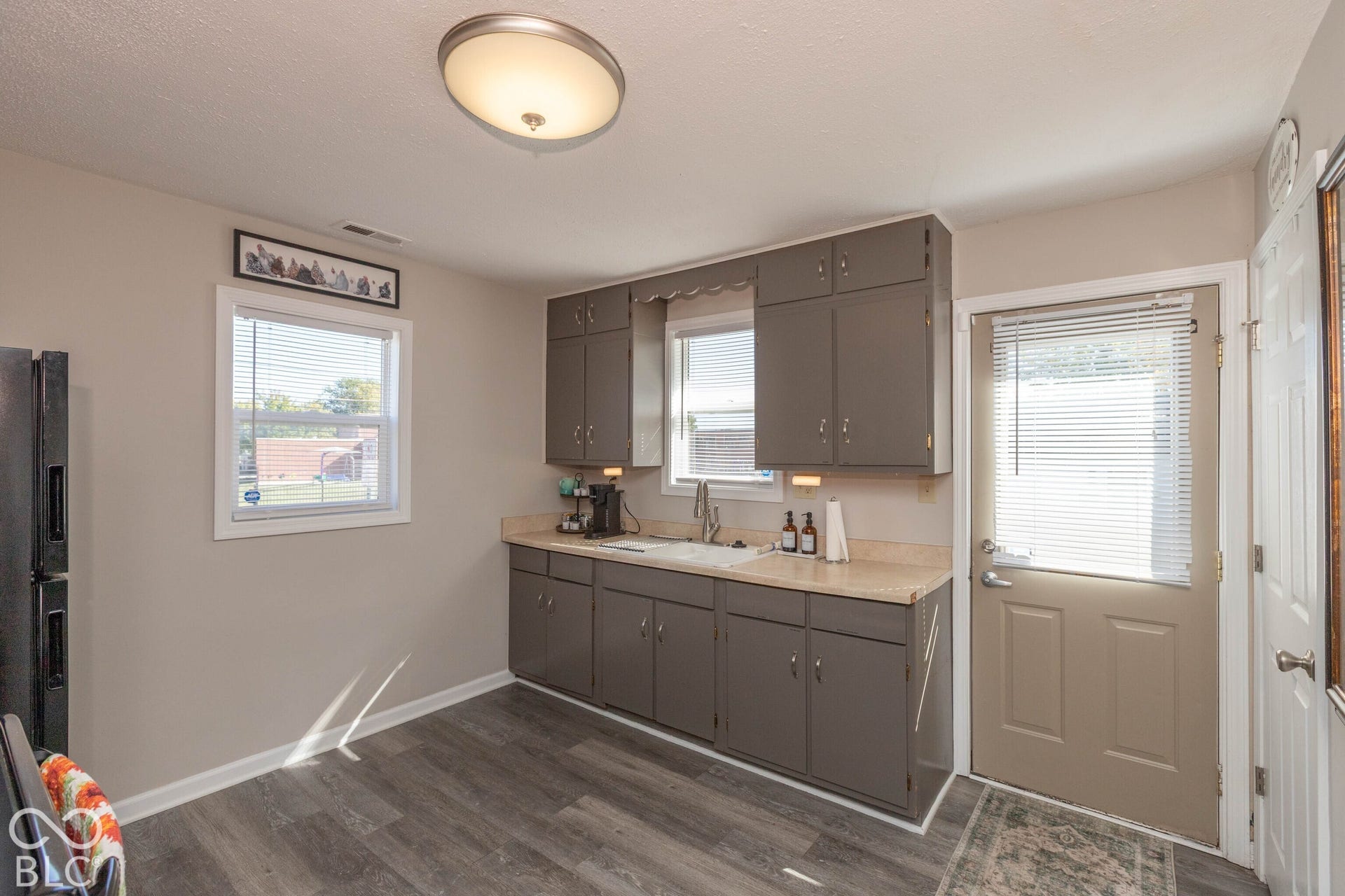 Kitchen featuring wood-finish flooring, two windows with blinds, gray cabinetry, and a rear exit door