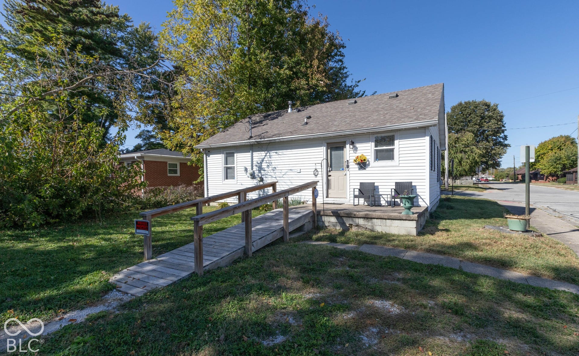 White siding exterior with a shingled roof, concrete porch, and a wooden access ramp