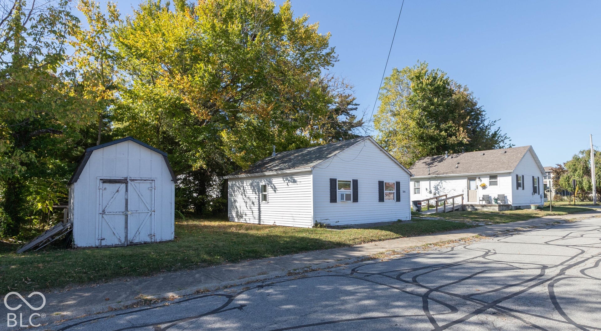 White exterior siding, dark window shutters, gabled roofline, and an additional storage shed