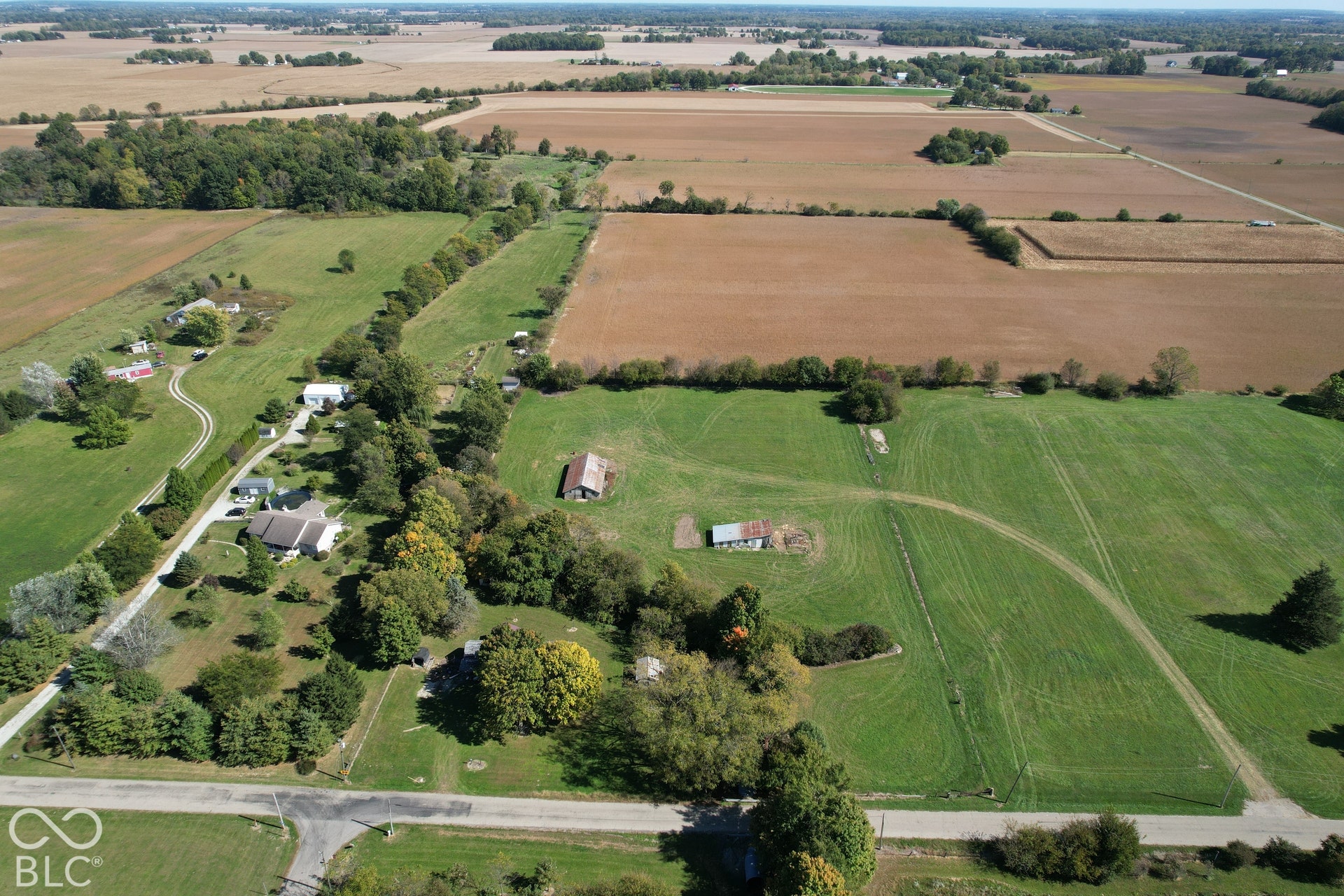 Expansive rural landscape featuring a mix of cultivated fields and green spaces, multiple residential structures, and established trees