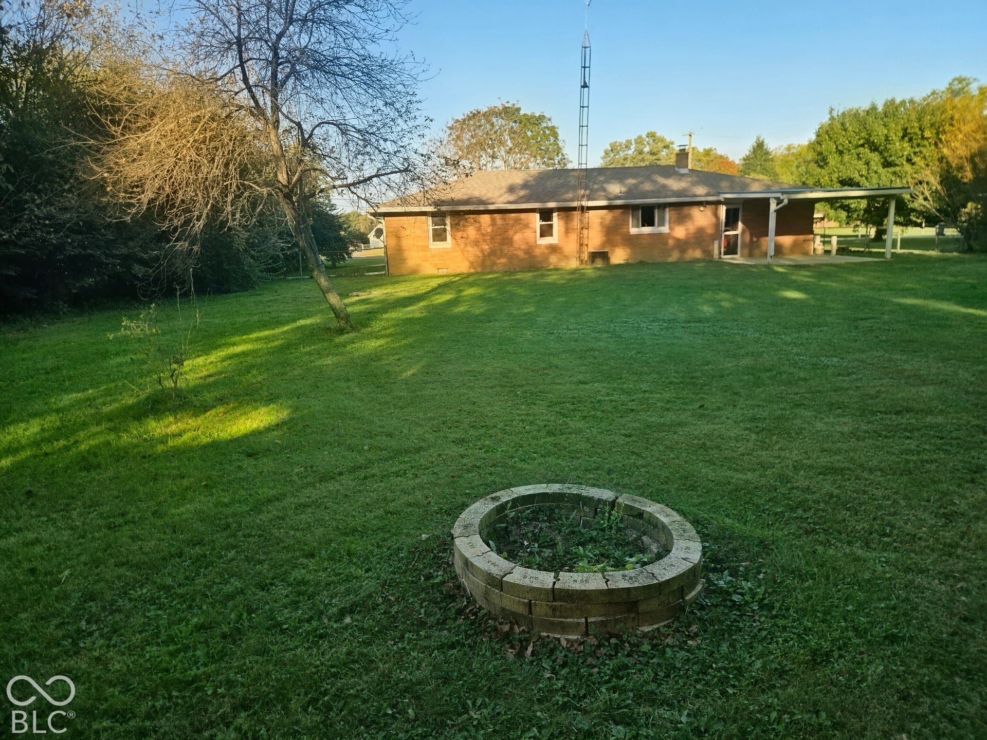 6720 S County Road 800 W, Daleville, IN 47334 Expansive rear lawn featuring a brick-built fire pit, mature trees, and a covered patio area