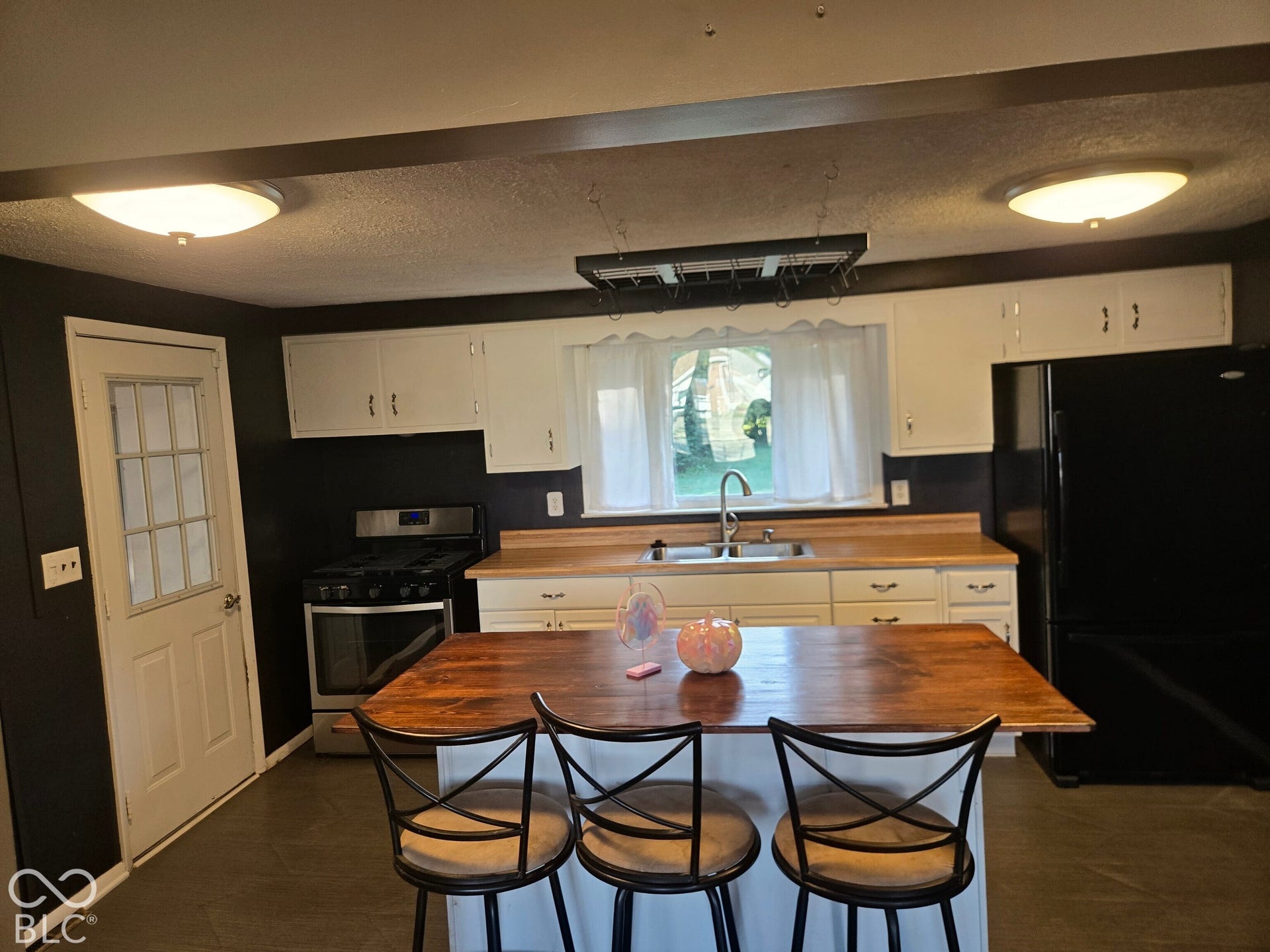 6720 S County Road 800 W, Daleville, IN 47334 Virtually Altered - Kitchen featuring a central island with wood-finish countertop, white cabinetry, stainless steel range, and a black refrigerator