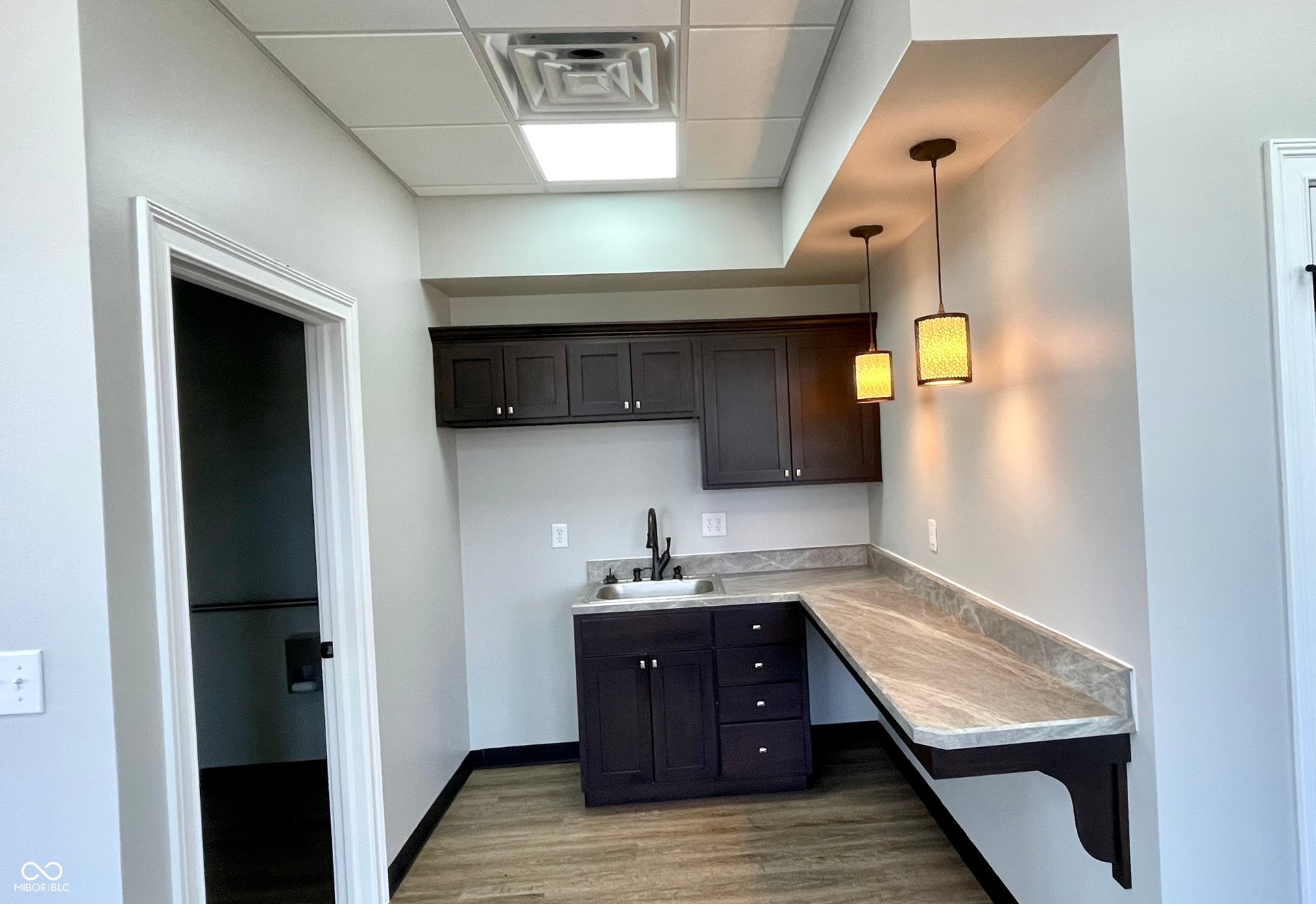 kitchen featuring light countertops, hanging light fixtures, dark wood finish cabinetry, and a paneled ceiling