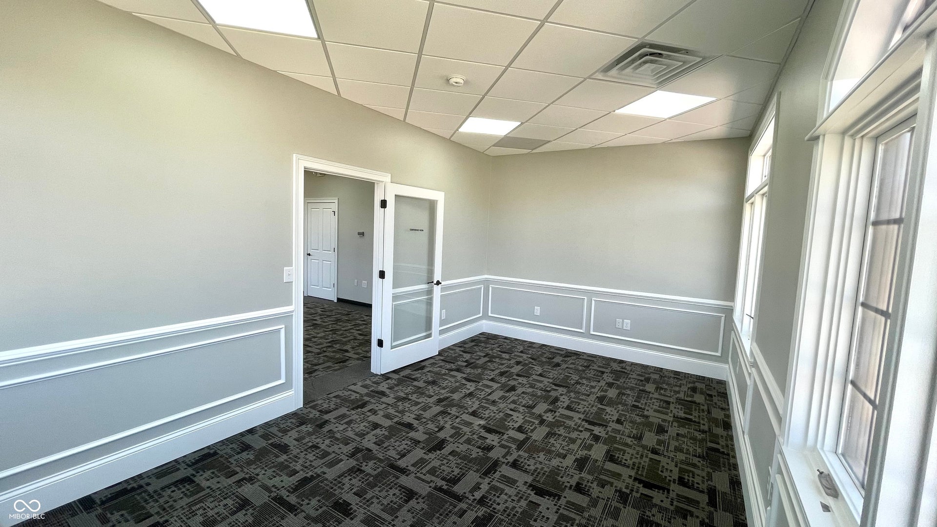 unfurnished room featuring dark carpet, a decorative wall, a paneled ceiling, and wainscoting