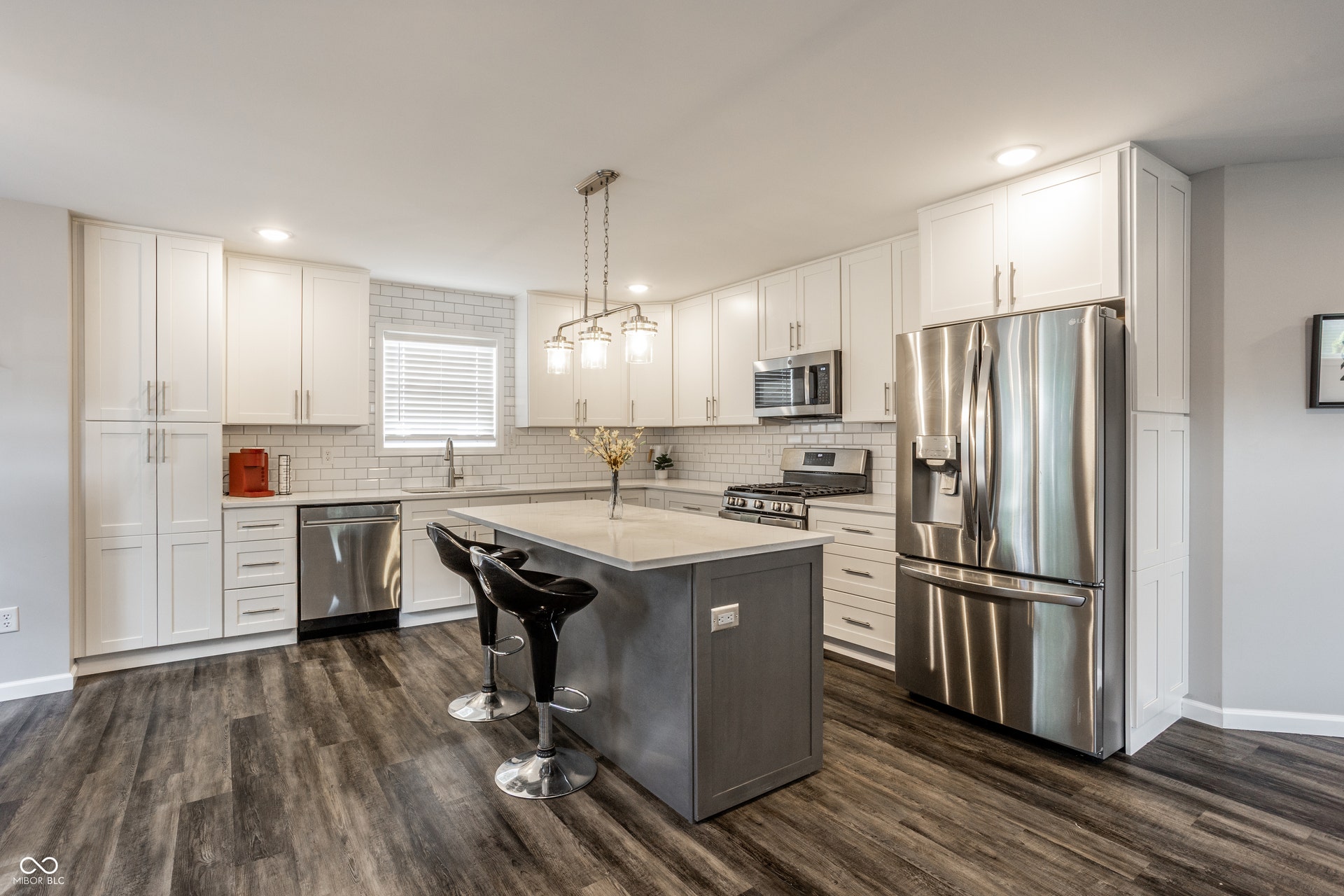 2323 E 57th Street, Indianapolis, IN 46220 Kitchen featuring white cabinetry, gray center island, stainless steel appliances, subway tile backsplash, and wood-finish flooring