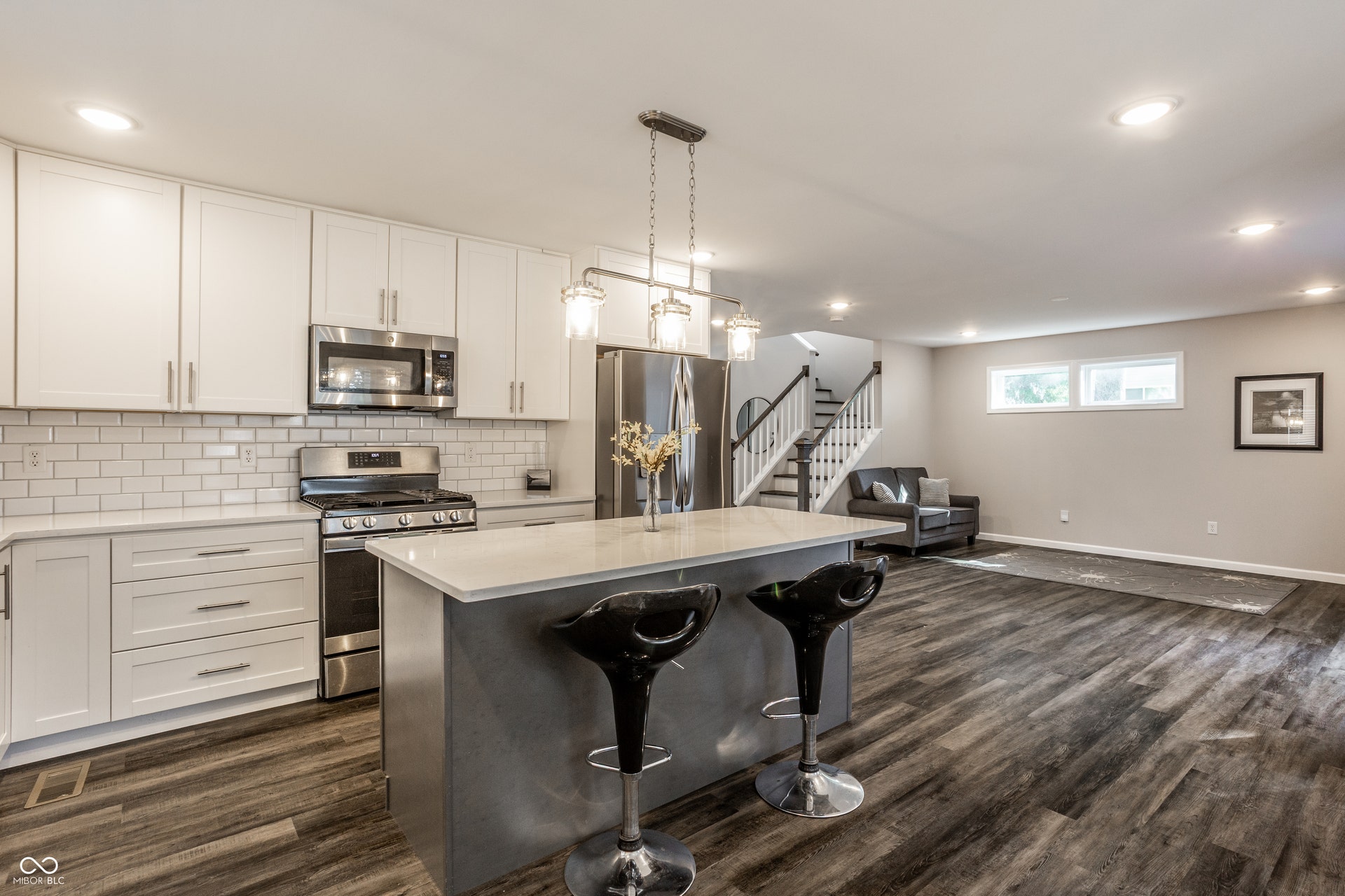 2323 E 57th Street, Indianapolis, IN 46220 Kitchen featuring white cabinetry, stainless steel appliances, a subway tile backsplash, a center island with countertop seating, and wood-finish flooring