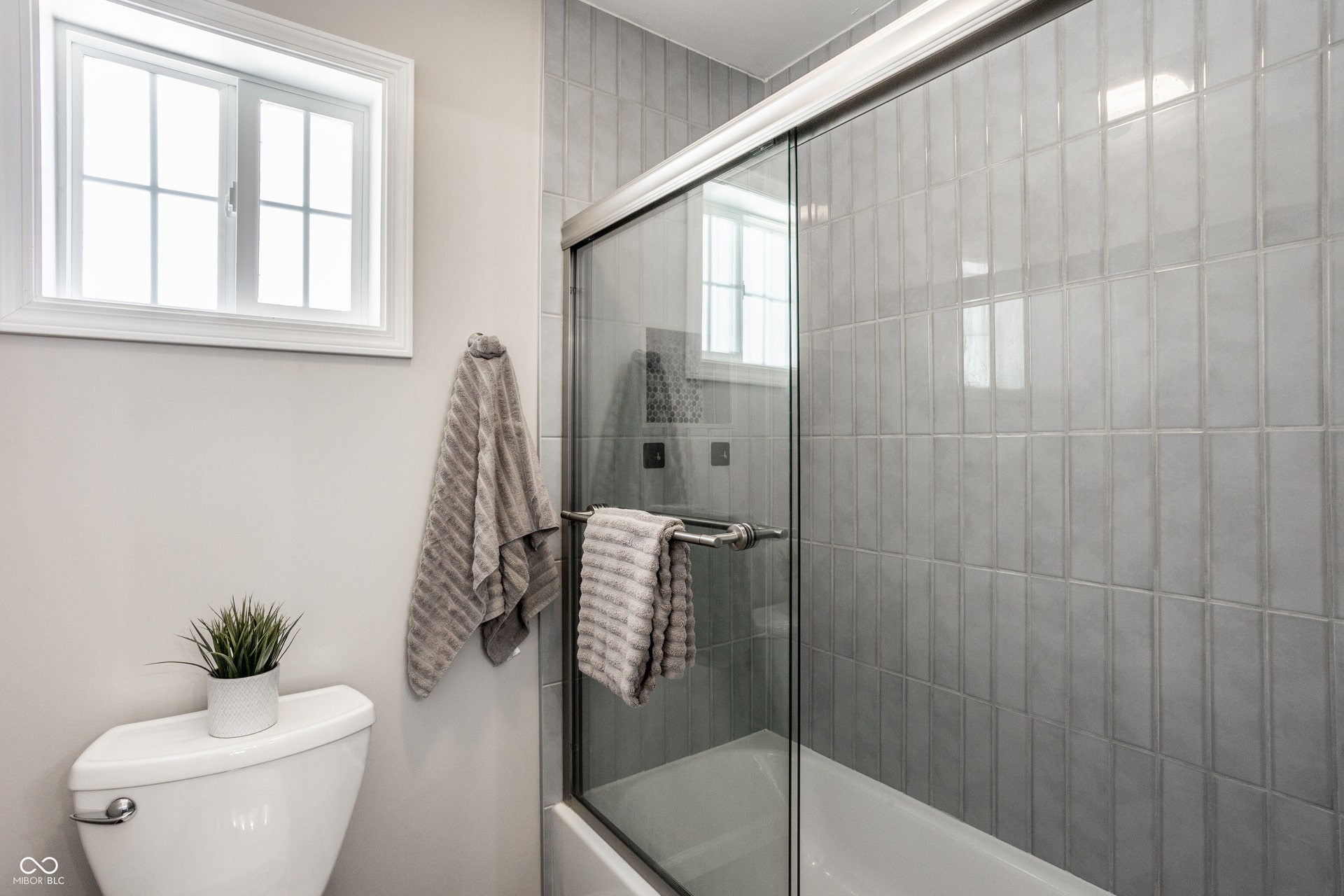 2323 E 57th Street, Indianapolis, IN 46220 White-framed window, ceramic tile shower surround, glass shower enclosure, built-in bathtub, and commode