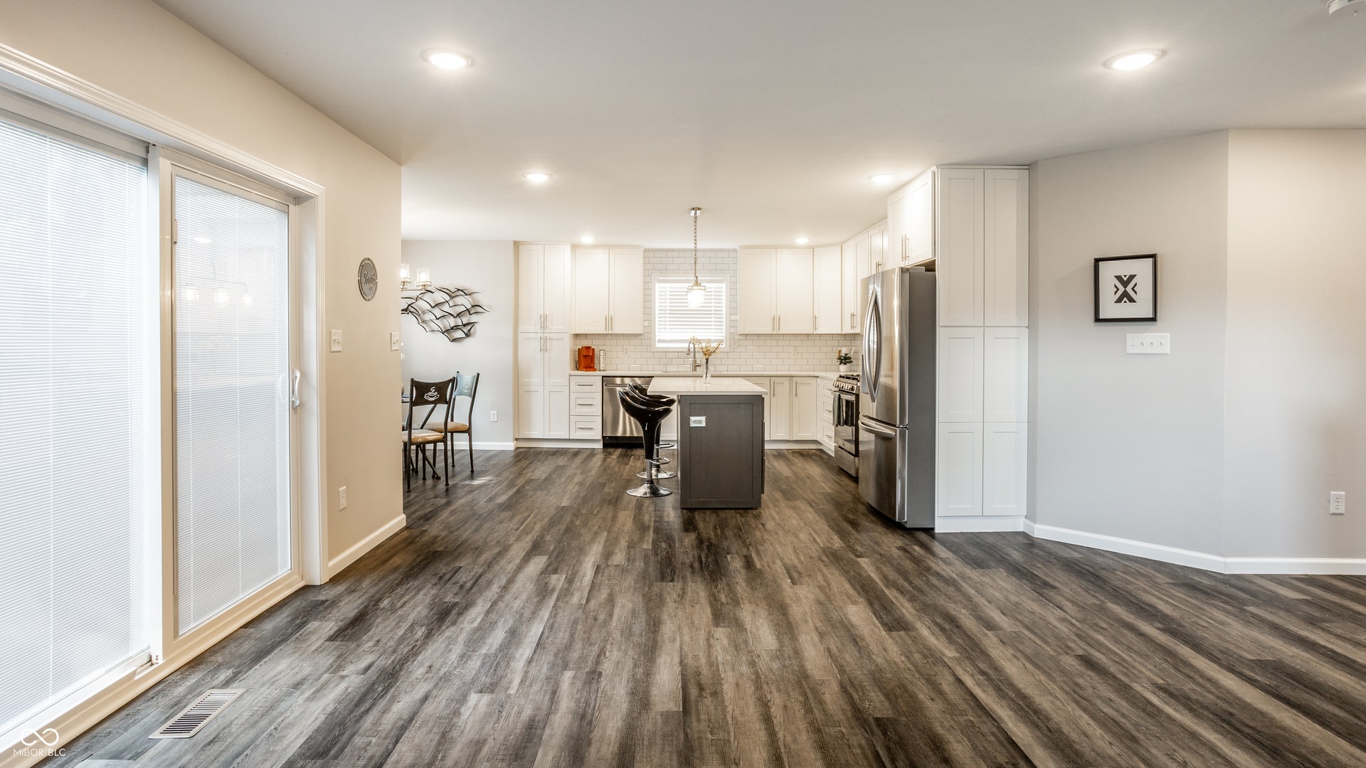 2323 E 57th Street, Indianapolis, IN 46220 Open-concept living space featuring dark wood-finish flooring throughout, white cabinetry with stainless steel appliances, a center island with seating, recessed lighting, and sliding glass doors with natural light access