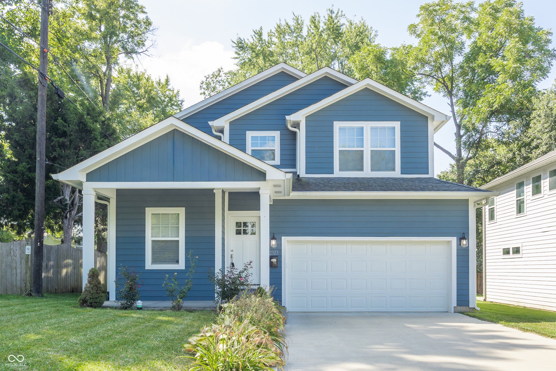 2323 E 57th Street, Indianapolis, IN 46220 Two-story residence featuring blue siding, a covered entry porch, an attached garage, a concrete driveway, and a fenced side yard