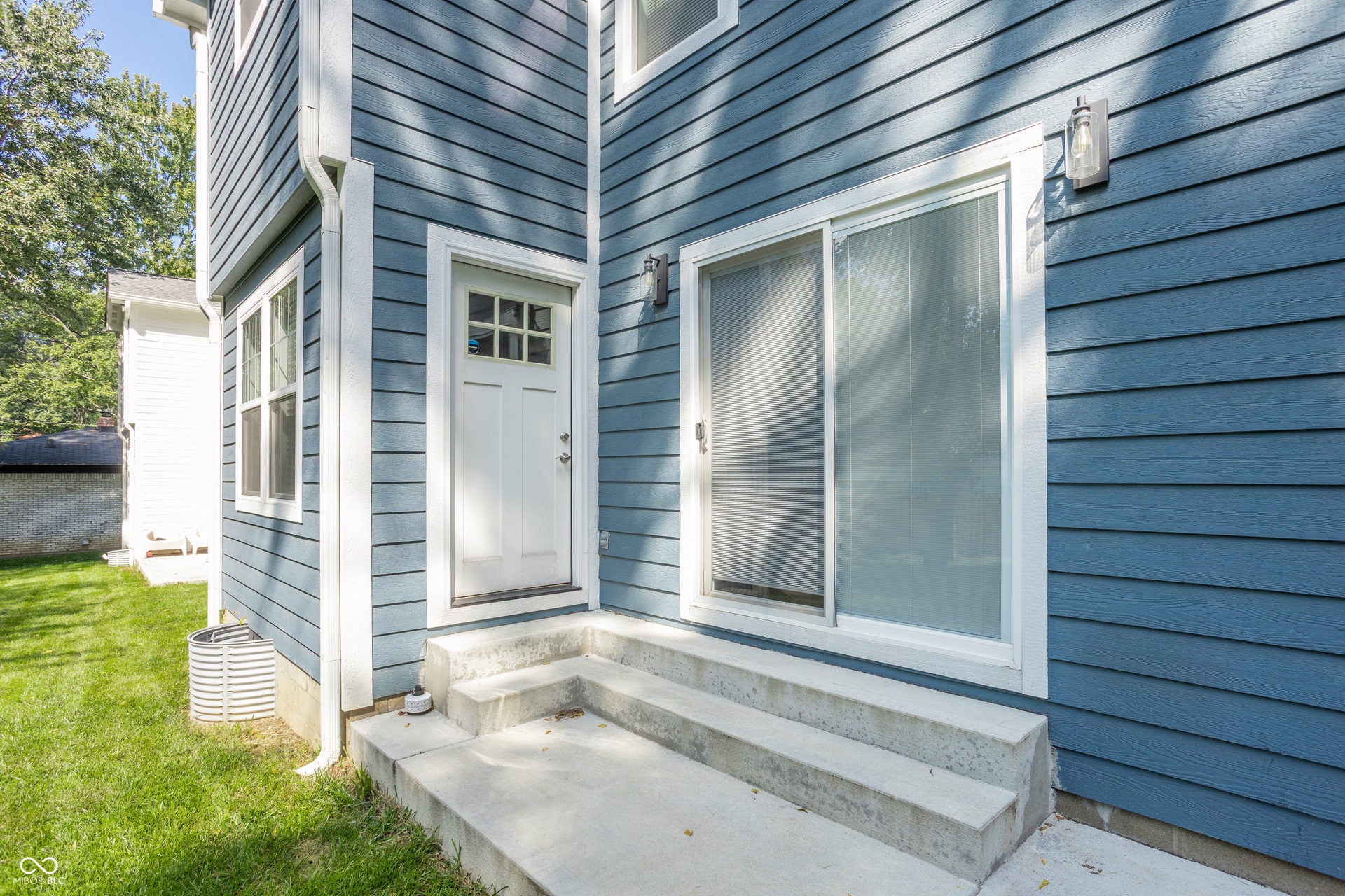 2323 E 57th Street, Indianapolis, IN 46220 Blue horizontal siding exterior with white trim, concrete patio, white paneled door, and sliding glass door