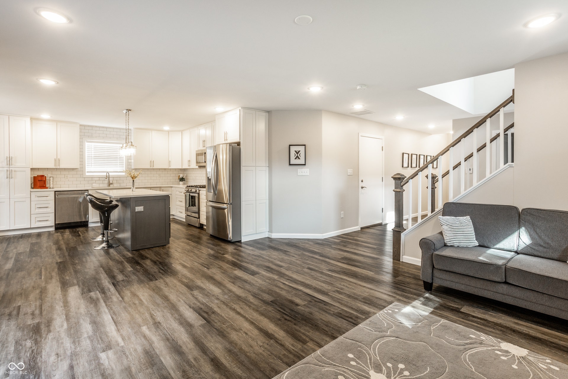 2323 E 57th Street, Indianapolis, IN 46220 Wood-finish flooring throughout, bright white kitchen cabinetry, stainless steel appliances, central kitchen island, and a staircase with white balusters
