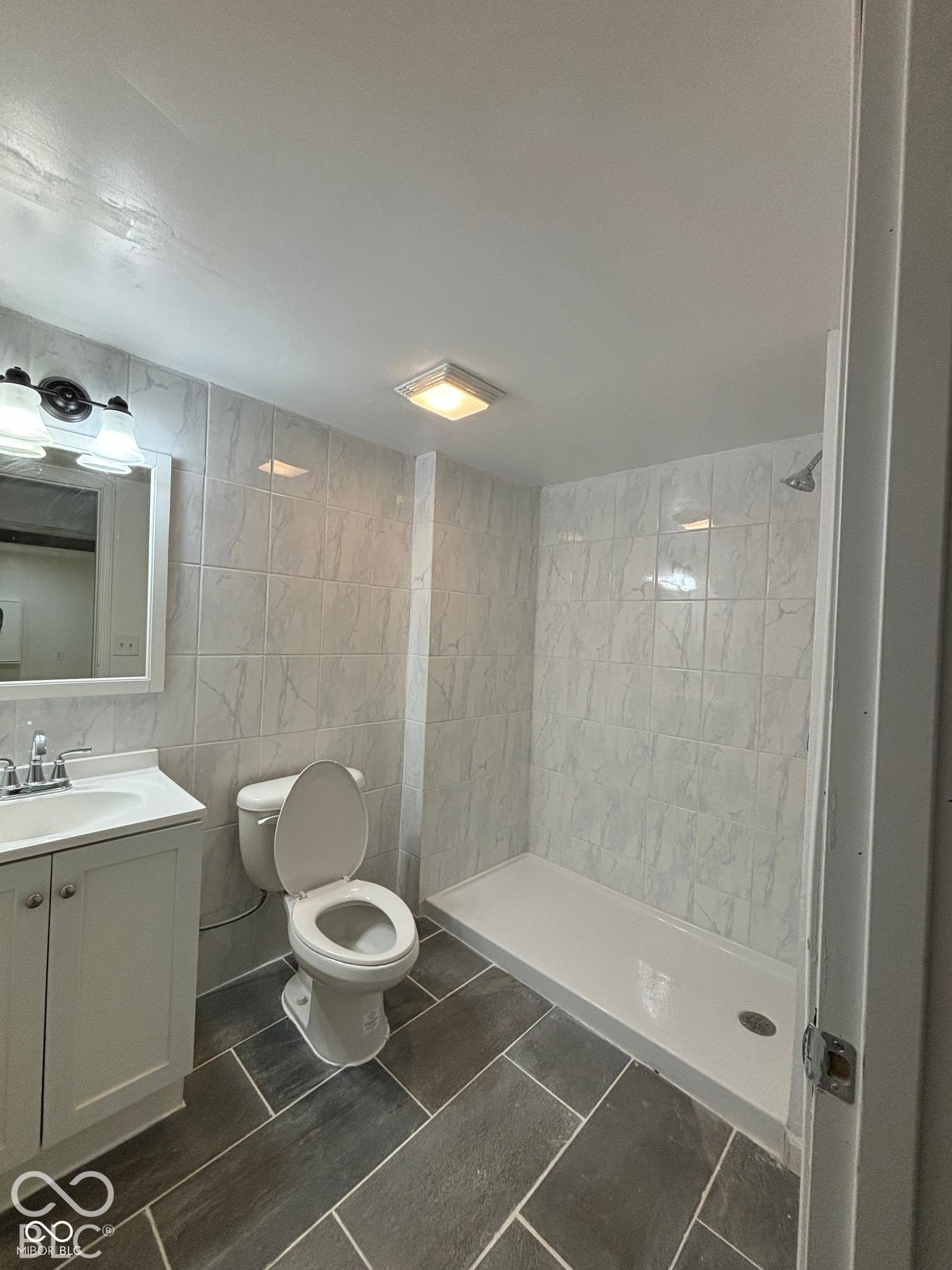 1345 Carroll White Drive, Indianapolis, IN 46219 Bathroom featuring a vanity with an integrated sink, a built-in shower, tiled walls, and rectangular floor tiles