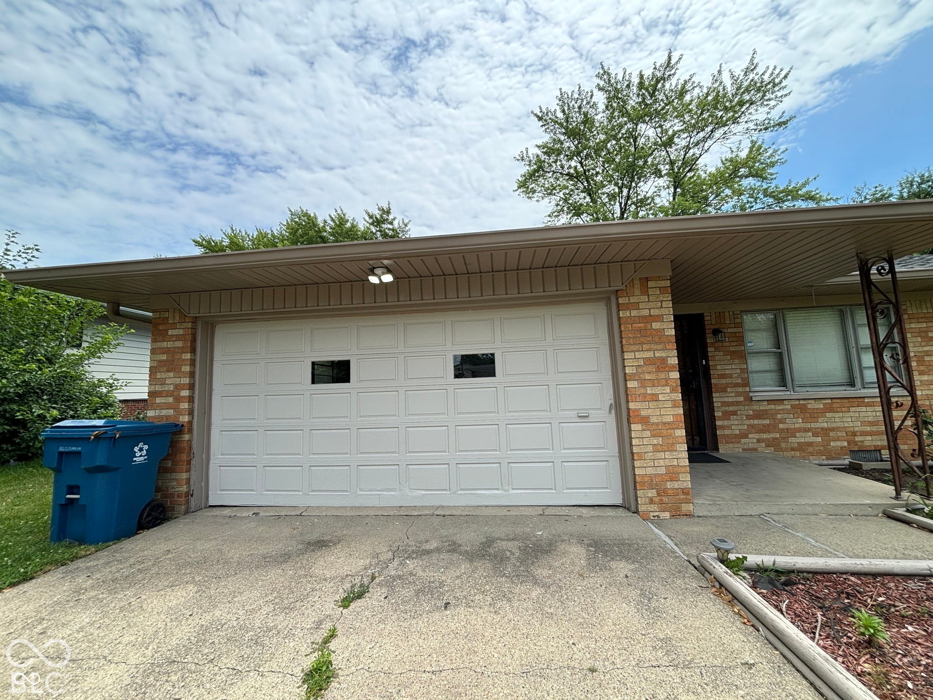 1345 Carroll White Drive, Indianapolis, IN 46219 Brick exterior with a white panel garage door, integrated garage lighting, and a concrete driveway