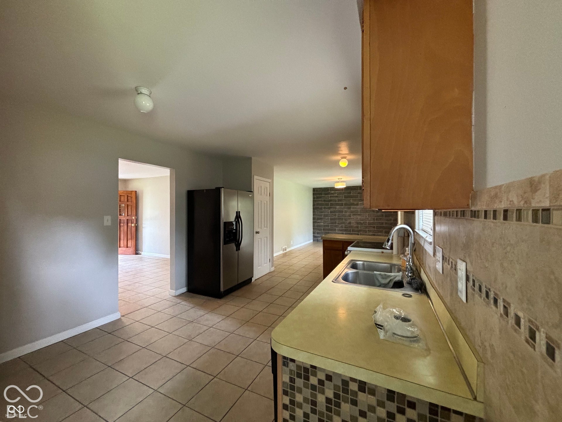 1345 Carroll White Drive, Indianapolis, IN 46219 Kitchen featuring wood-finish cabinetry, a double basin stainless steel sink, and a tiled backsplash