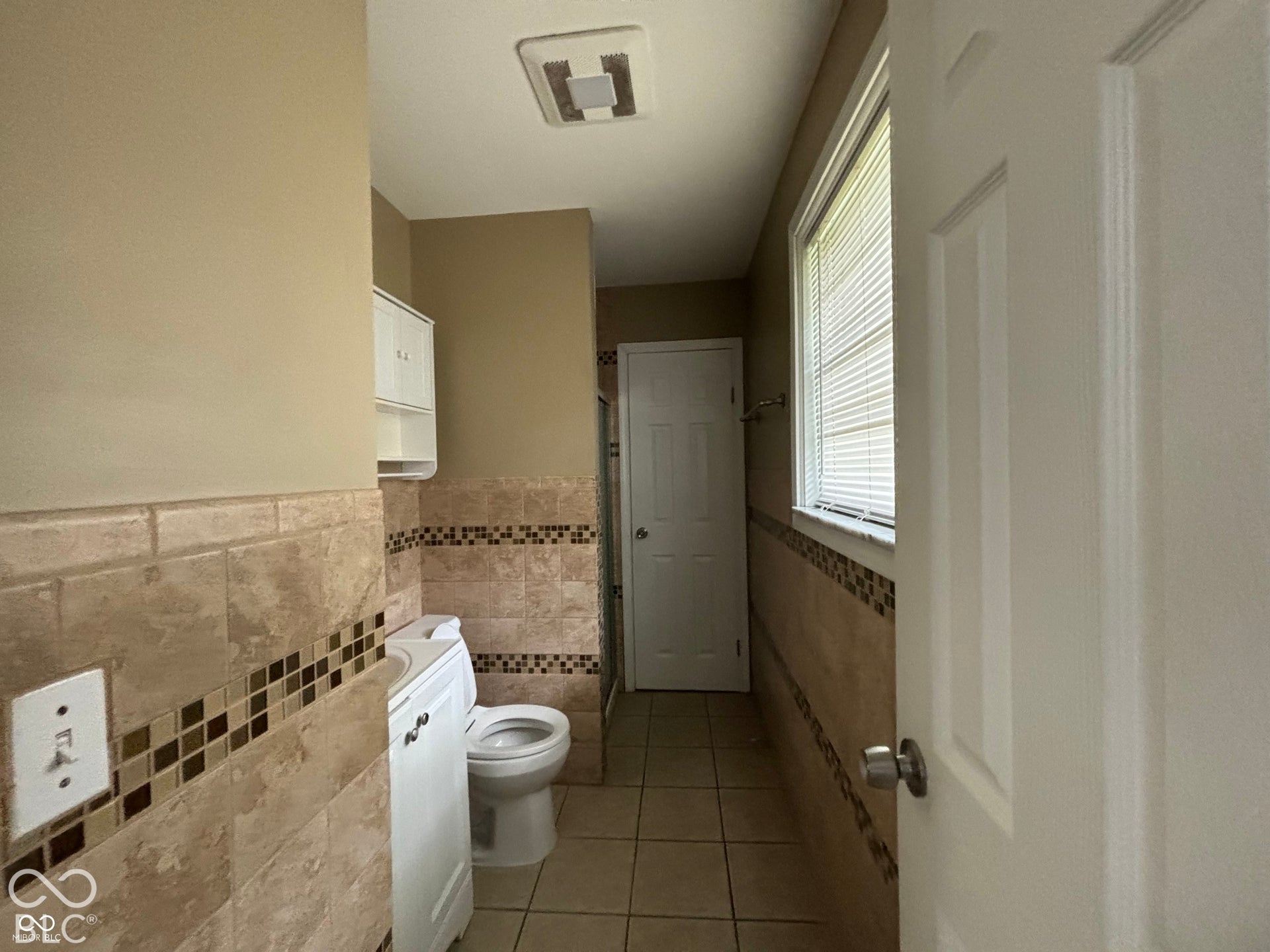 1345 Carroll White Drive, Indianapolis, IN 46219 Tiled walls with decorative mosaic accents, window with horizontal blinds, tiled flooring, built-in wall cabinet, and ceiling-mounted exhaust fan