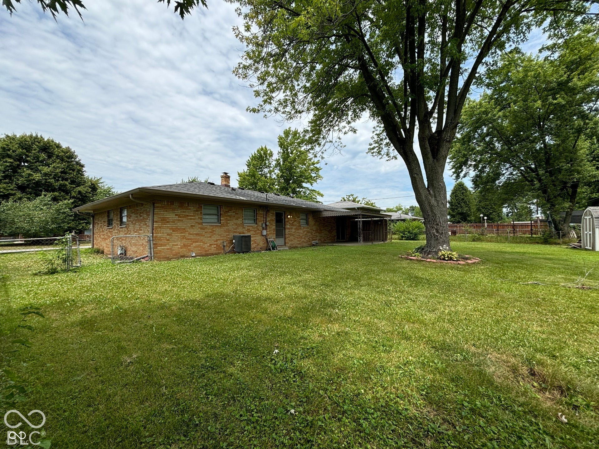 1345 Carroll White Drive, Indianapolis, IN 46219 Expansive grassy area featuring mature trees and a brick-sided residence with a covered patio