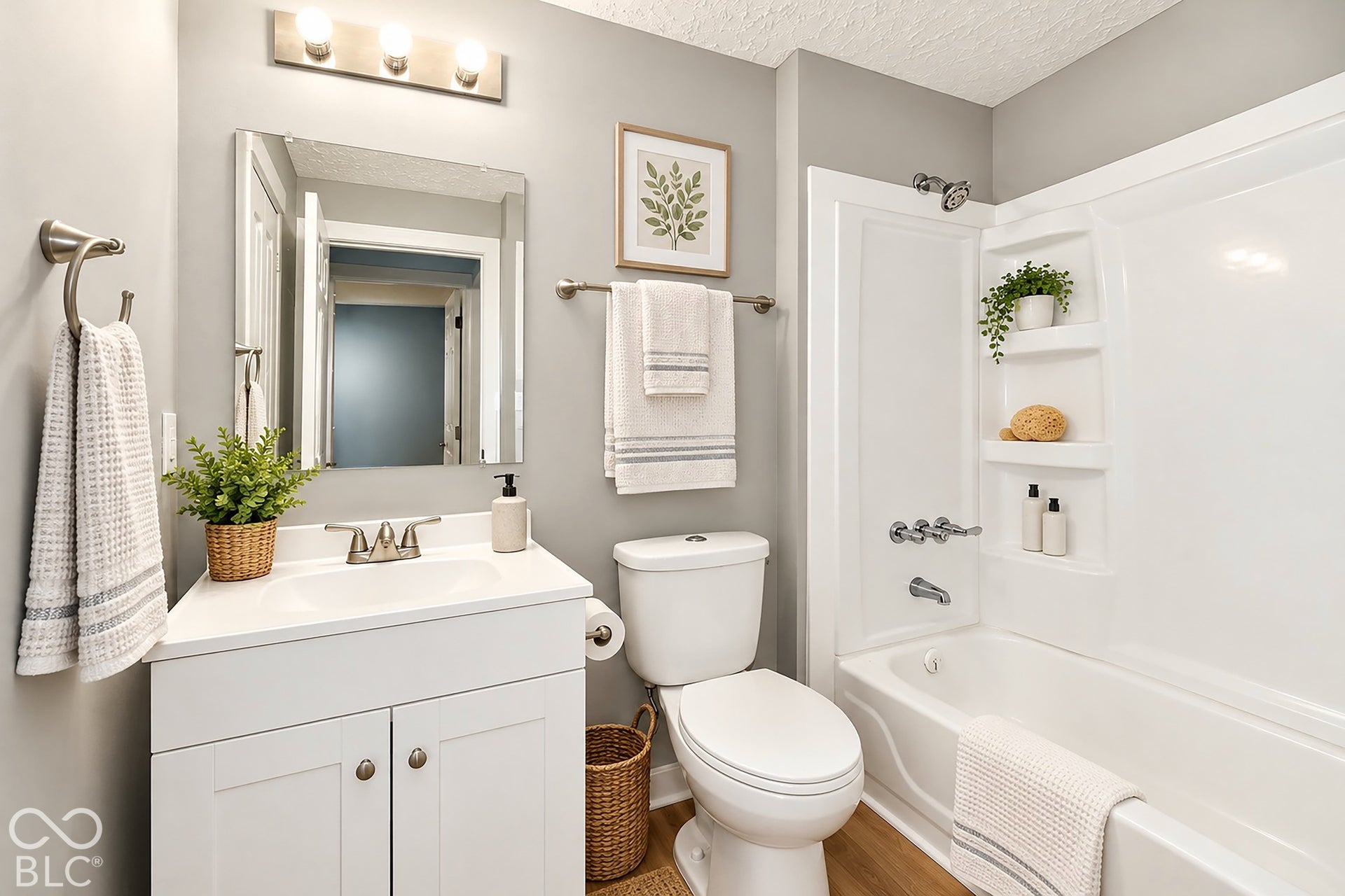 Virtually Altered - White vanity cabinet with an integrated sink and countertop, polished chrome fixtures, wall-mounted vanity lighting, and a white acrylic shower-tub surround featuring built-in recessed shelving
