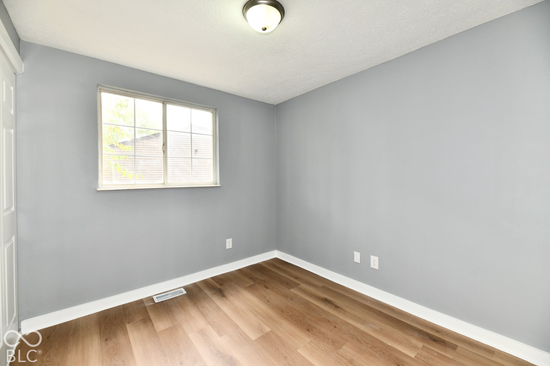 Neutral interior space featuring wood-finish flooring, a sliding window, and a flush-mount ceiling light fixture