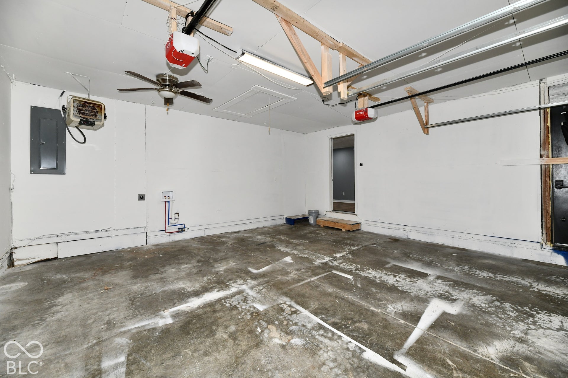 Garage interior featuring concrete flooring, an overhead ceiling fan, dual automated garage door openers, and plumbing hookups