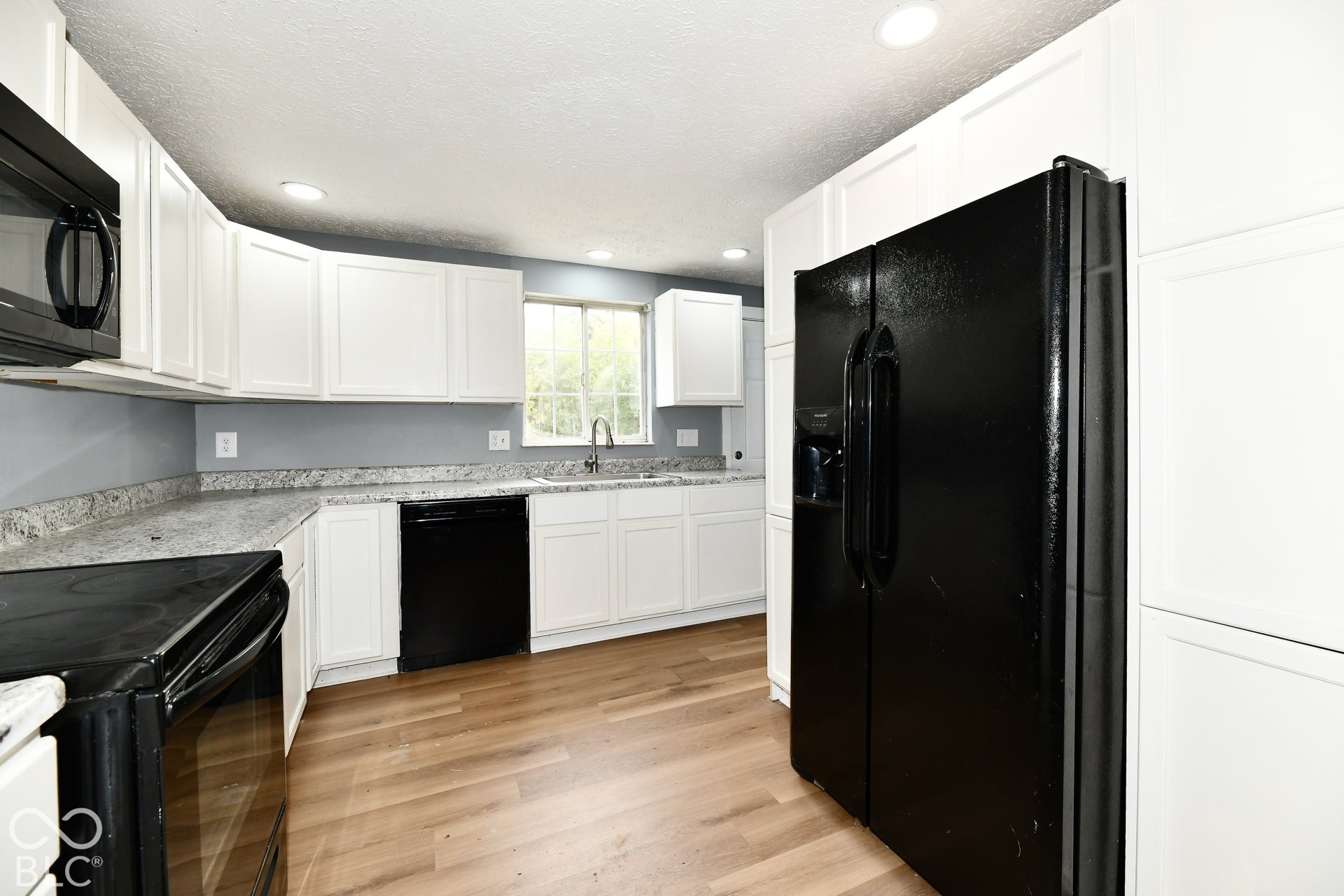 Kitchen featuring white shaker-style cabinetry, stone-finish countertops, black appliance suite, single-basin stainless steel sink with pull-down faucet, and wood-finish flooring