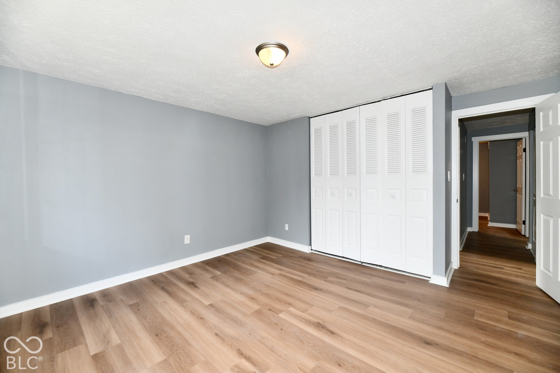 Room featuring wood-finish flooring, neutral wall paint, and a floor-to-ceiling closet with white louvered doors