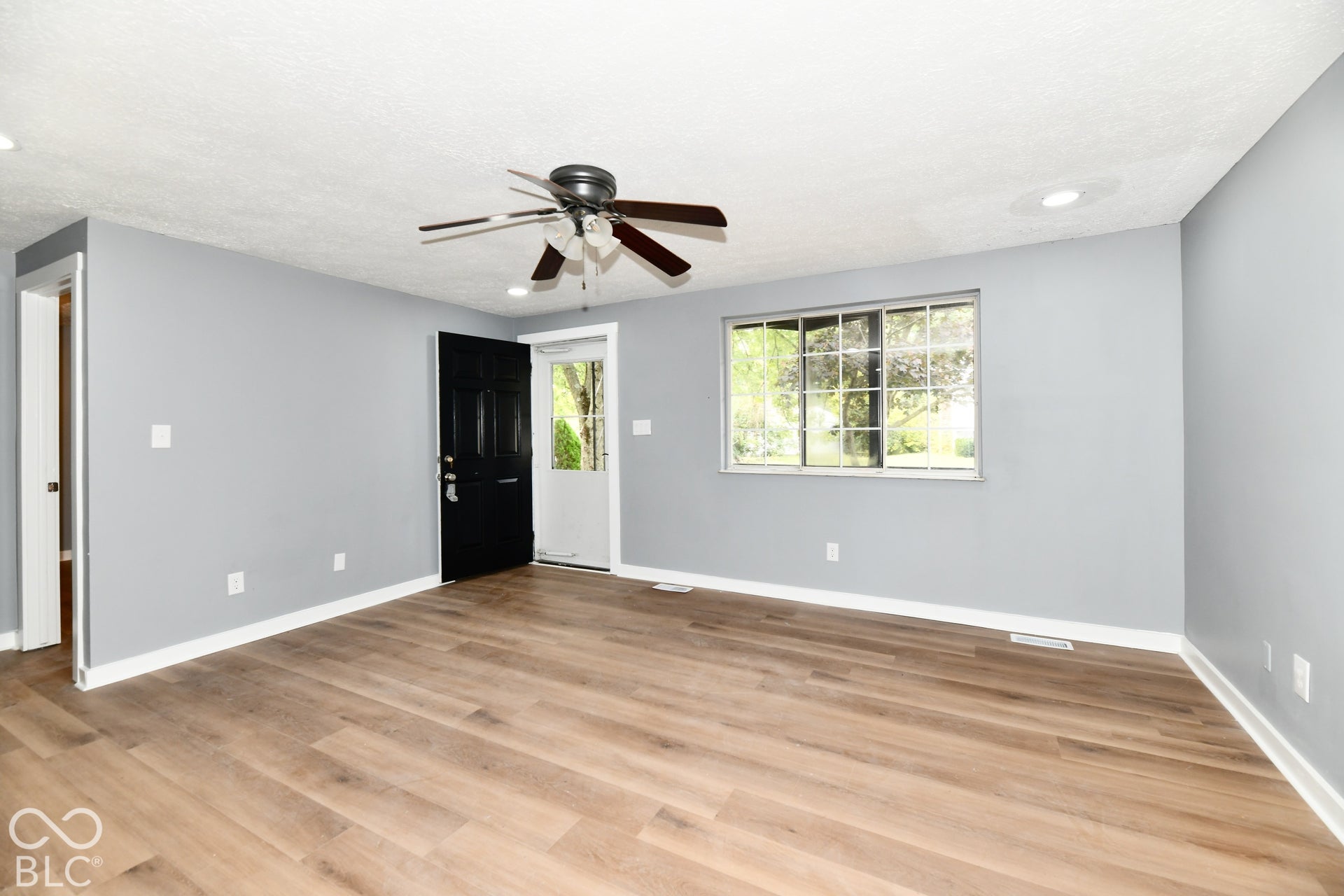 Interior space featuring wood-finish flooring, neutral wall paint, a multi-blade ceiling fan with integrated lighting, recessed lighting, and a window with exterior pane detailing