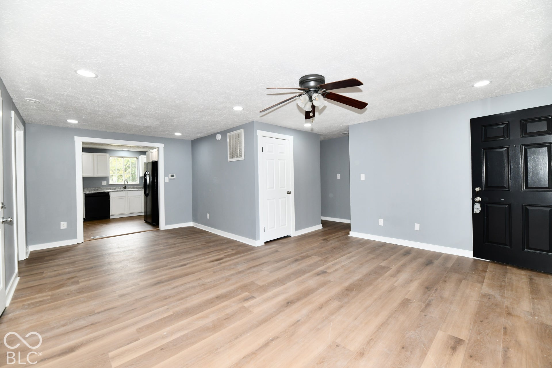 Open floor plan featuring wood-finish flooring, recessed lighting, a ceiling fan, and a six-panel black entry door