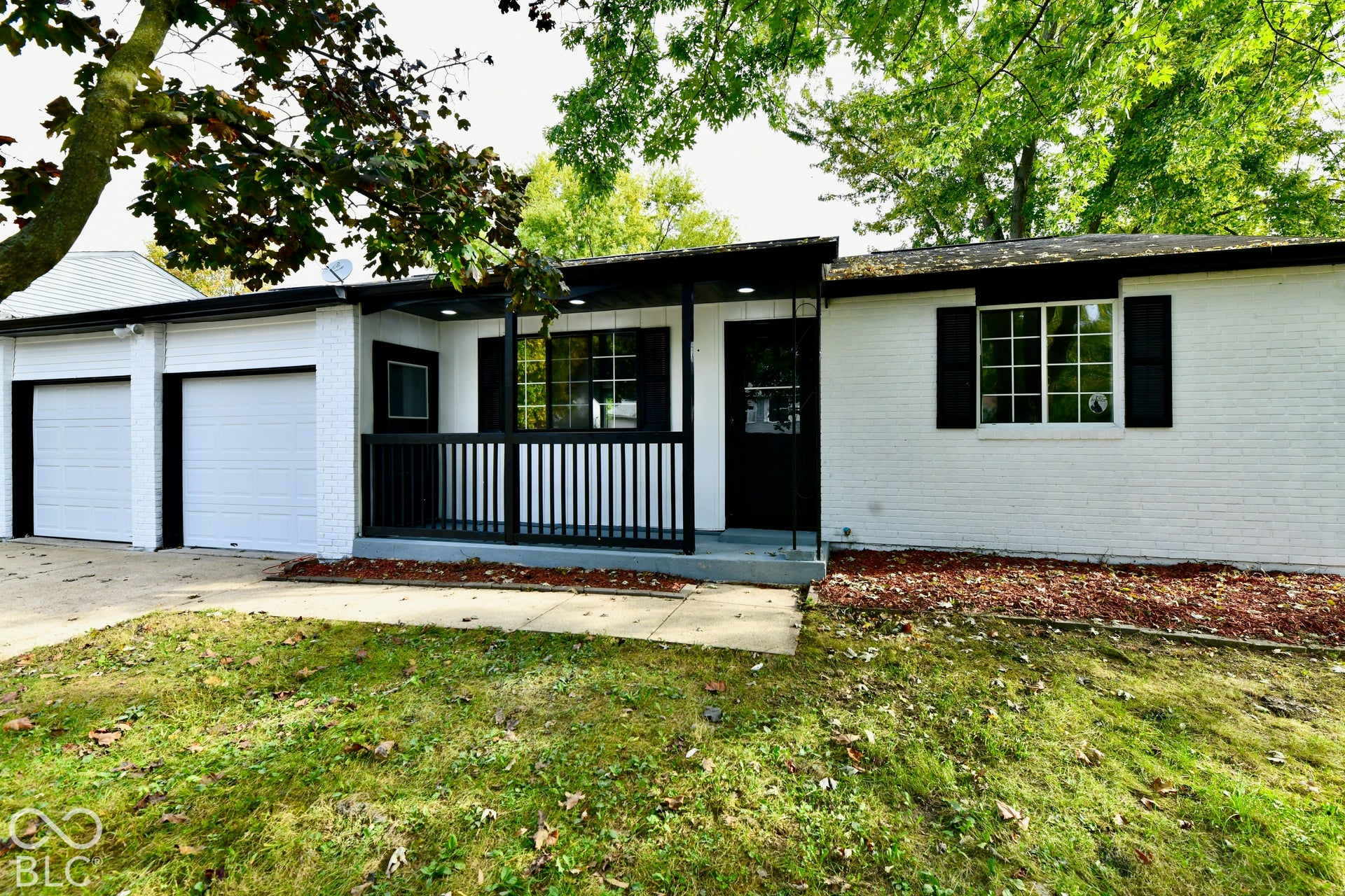 Painted brick exterior featuring a covered front porch with vertical railing, multi-pane windows with shutters, and a two-car garage