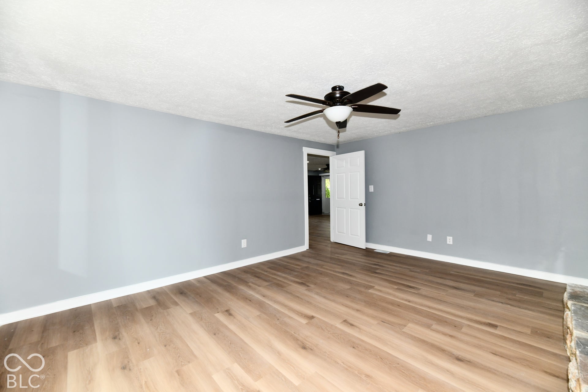 Neutral-toned interior featuring wood-finish flooring, a textured ceiling, a central ceiling fan with an integrated light fixture, and a six-panel interior door
