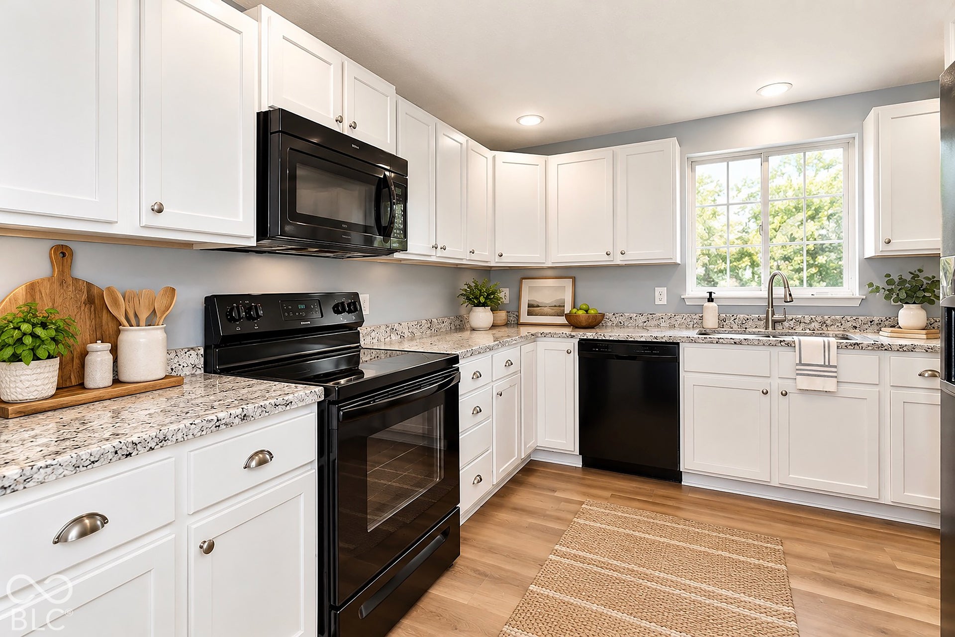 Virtually Altered - Kitchen featuring white shaker-style cabinetry, stone-patterned countertops, black appliances, a dual-basin stainless steel sink with a pull-down faucet, and wood-finish flooring