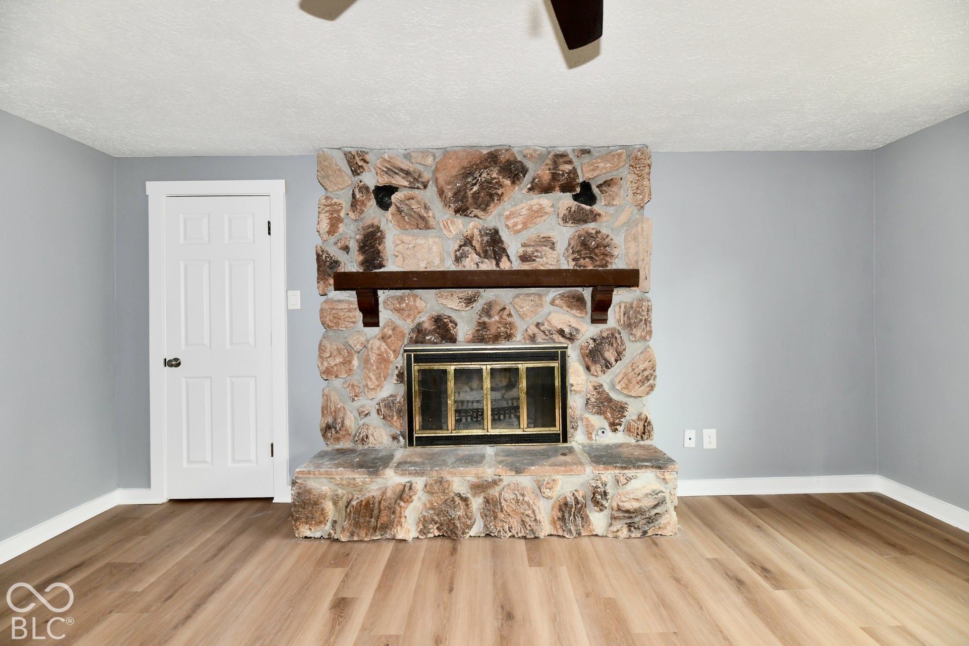 Floor-to-ceiling fieldstone fireplace with a substantial wood mantel, metal hearth surround, raised stone hearth, and wood-finish flooring