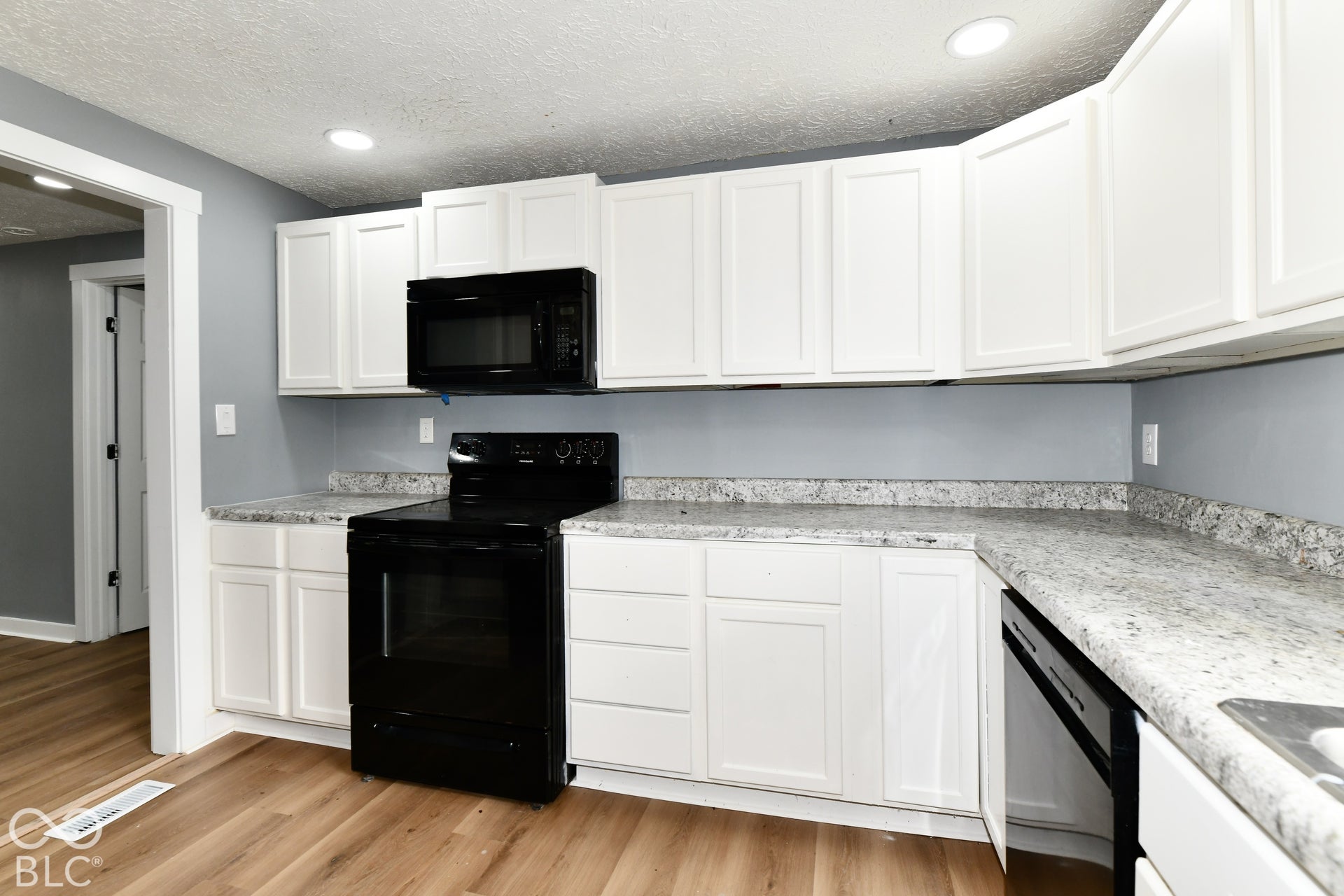 Kitchen featuring white shaker-style cabinetry, speckled stone-finish countertops, black built-in appliances, recessed lighting, and wood-finish flooring