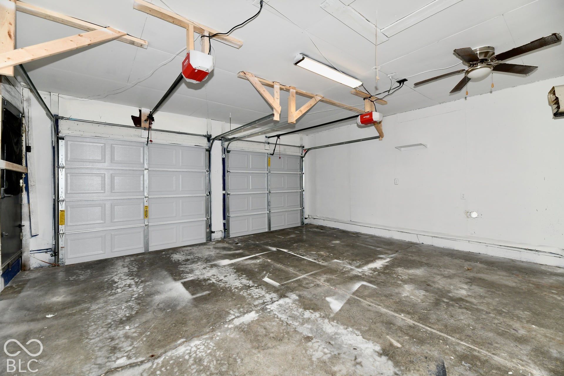 Two-car garage featuring dual overhead doors, concrete flooring, ceiling-mounted lighting, and a ceiling fan