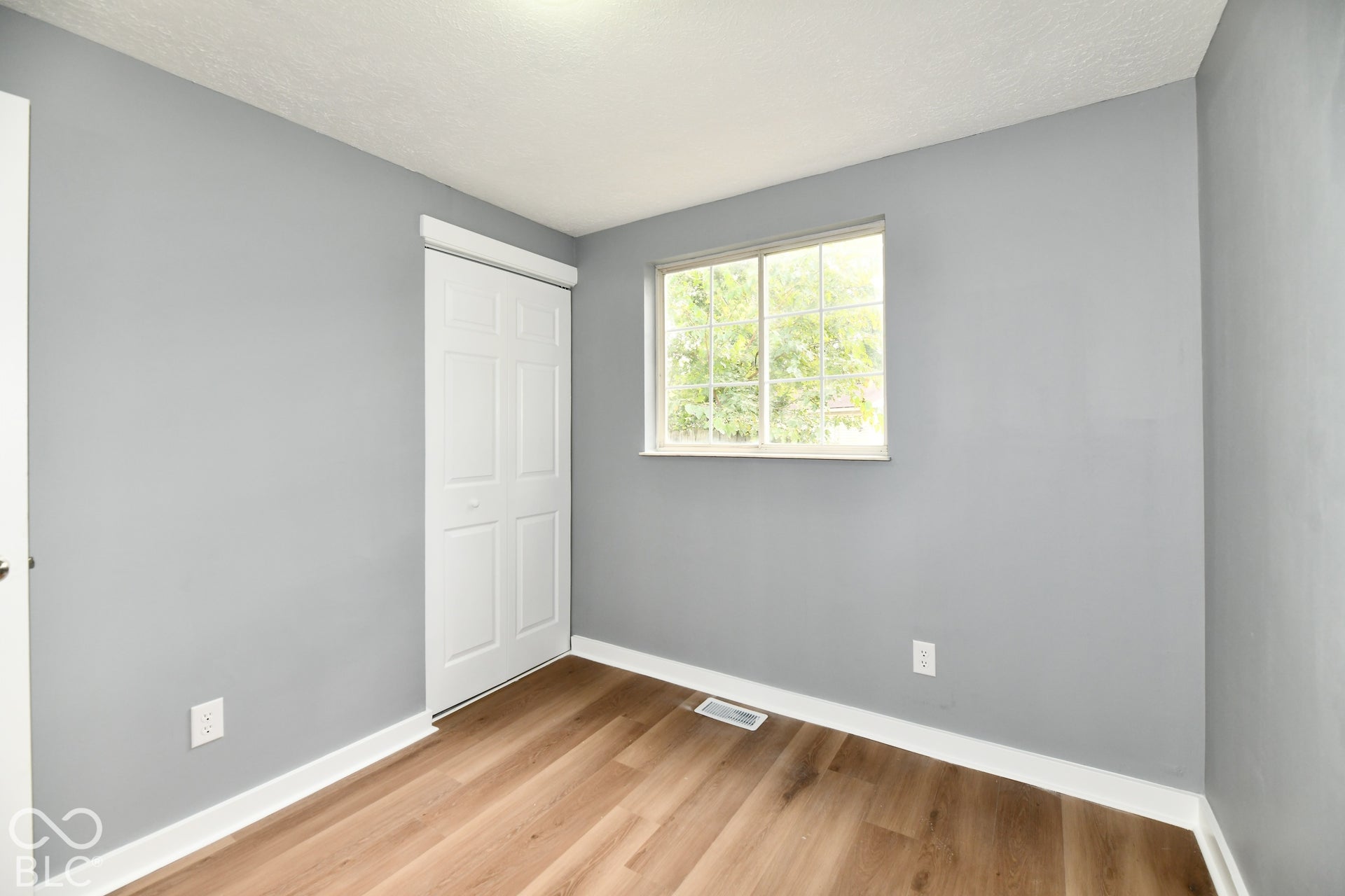 Neutral-toned interior space featuring wood-finish flooring, a sliding bi-fold closet door, and a horizontal window with grid muntins